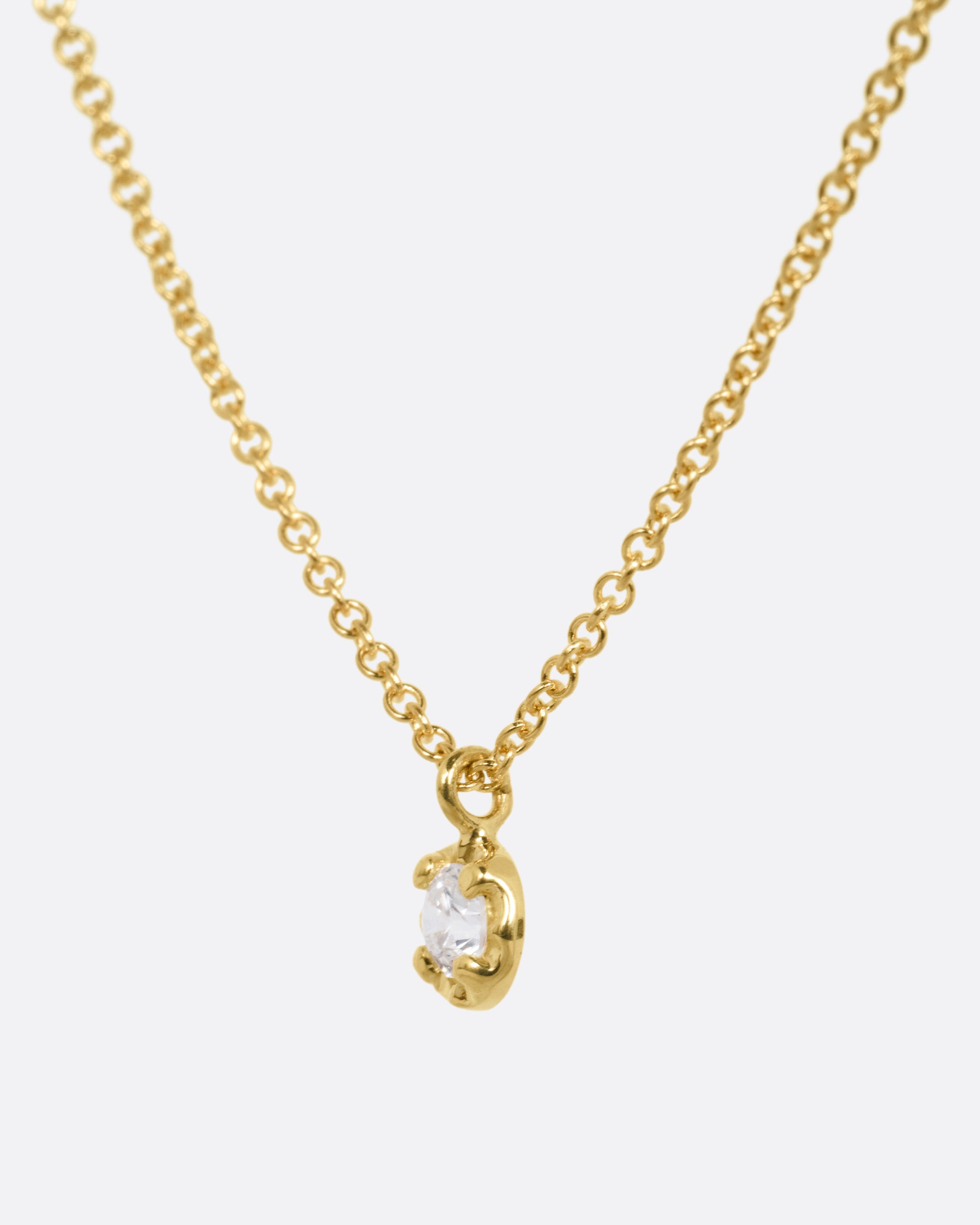 A yellow gold cable chain necklace with a  prong set white diamond, shown from the side.