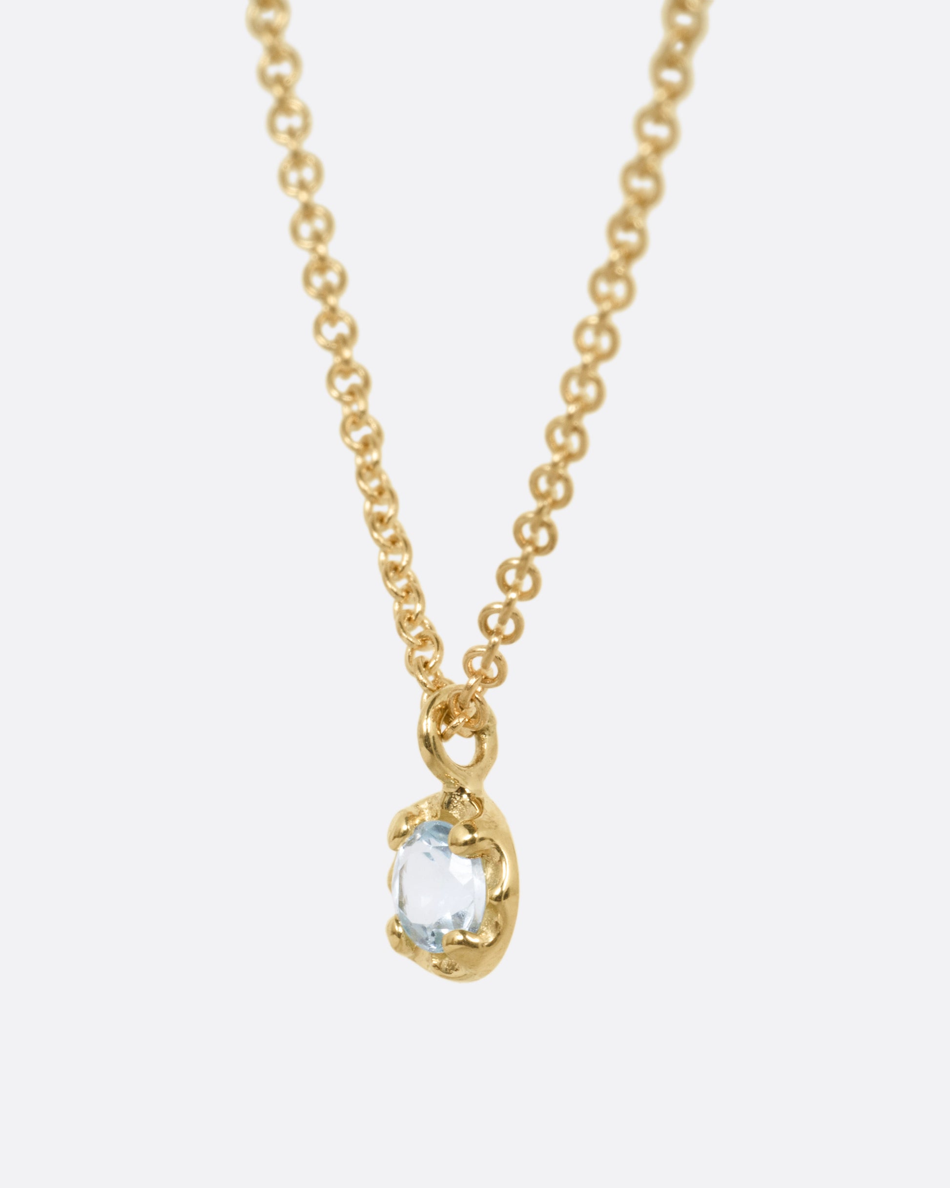 A yellow gold cable chain necklace with a  prong set aquamarine, shown from the side.