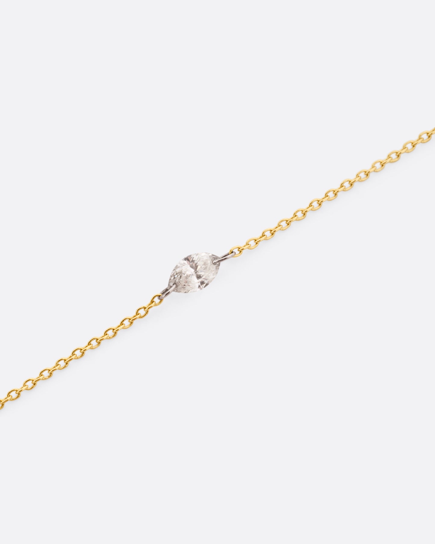 A close up of a yellow gold cable chain bracelet with platinum jump rings and a free set marquise diamond. 
