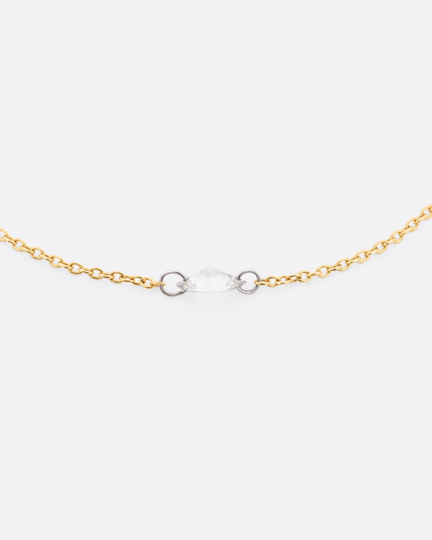 A close up of a yellow gold cable chain bracelet with platinum jump rings and a free set marquise diamond. 