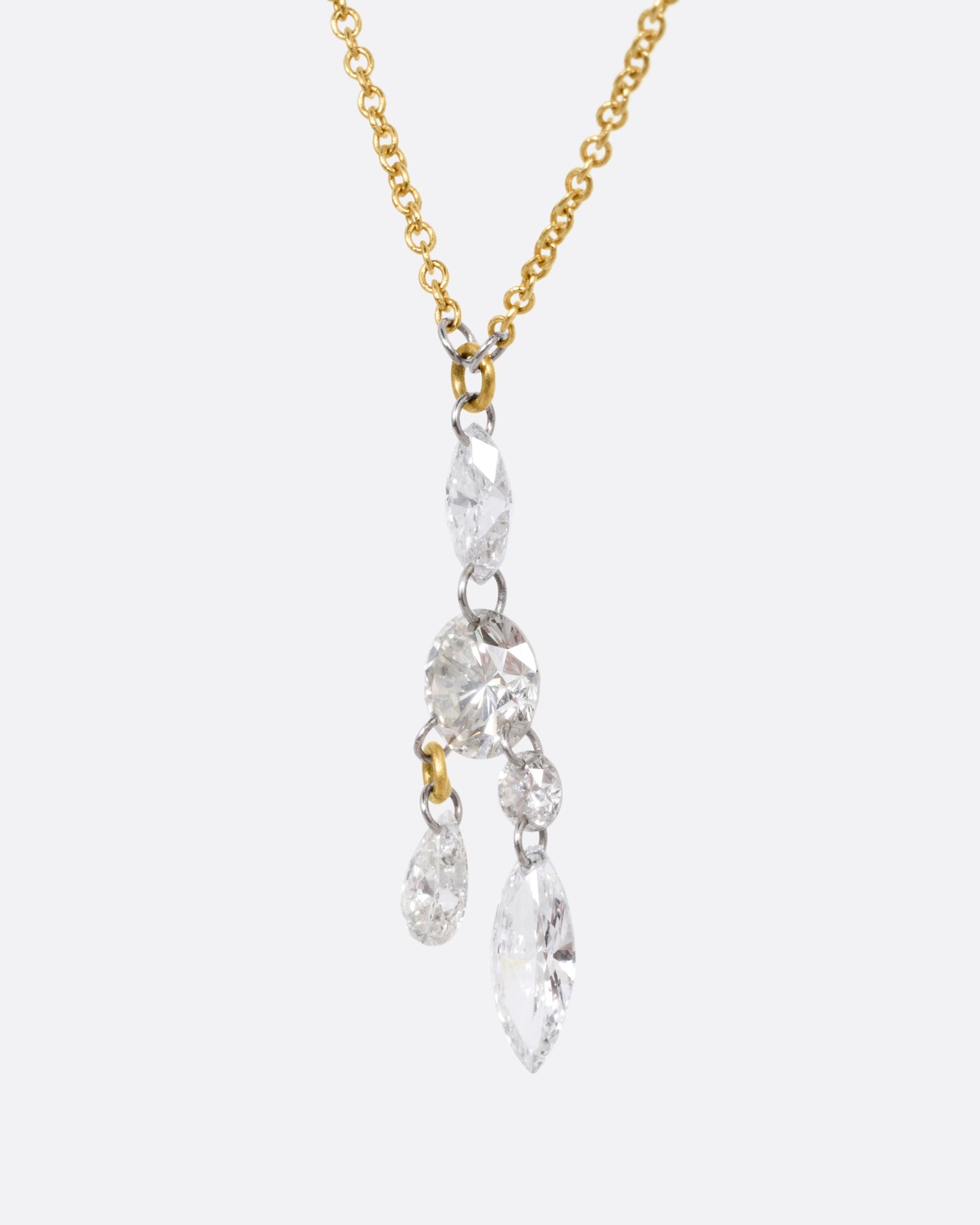 A yellow gold cable chain necklace with an arrangement of free set round, marquise, and pear shaped diamonds in platinum jump rings, shown from the side.
