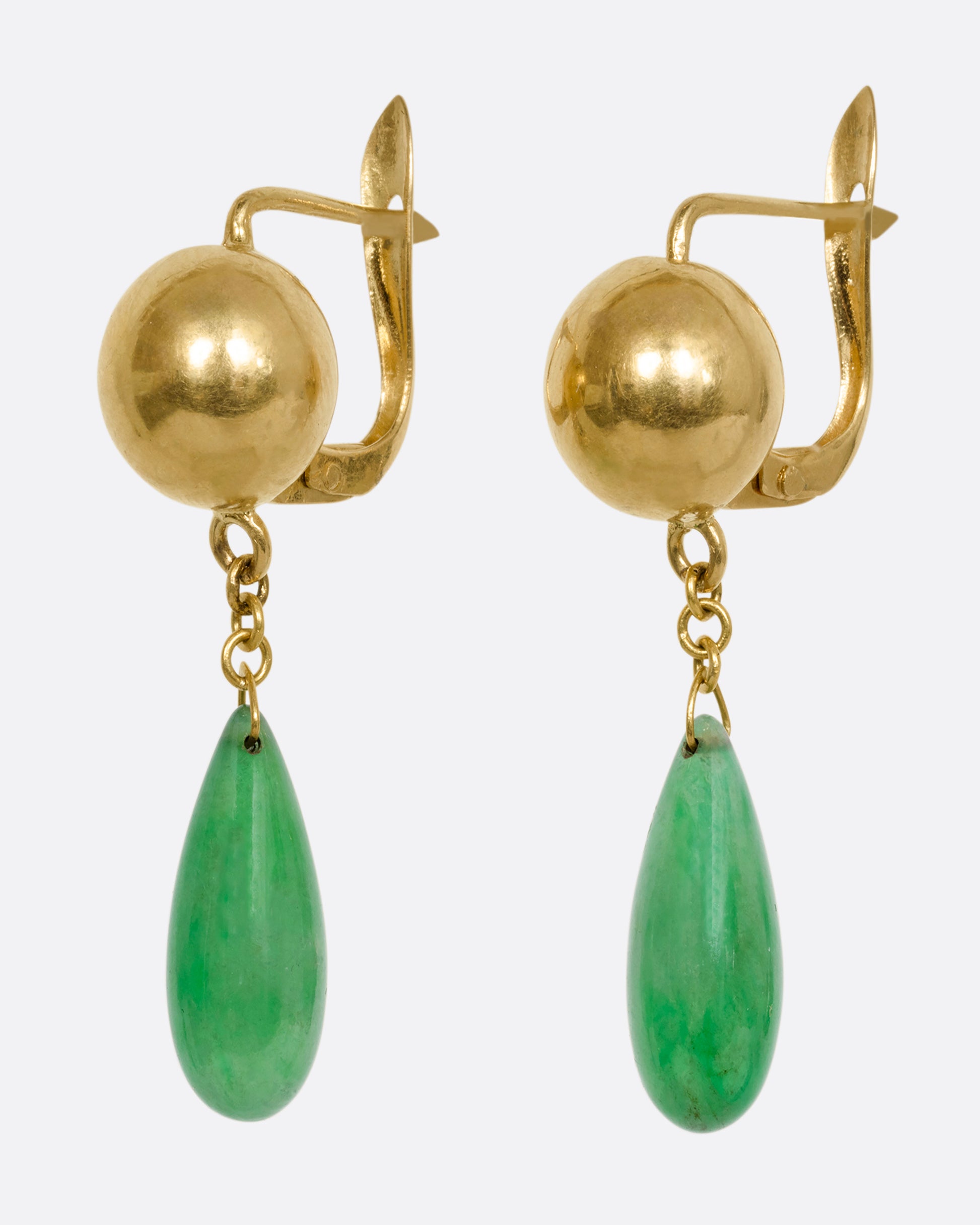 A pair of yellow gold ball earrings with teardrop jade drops. Shown from the side.