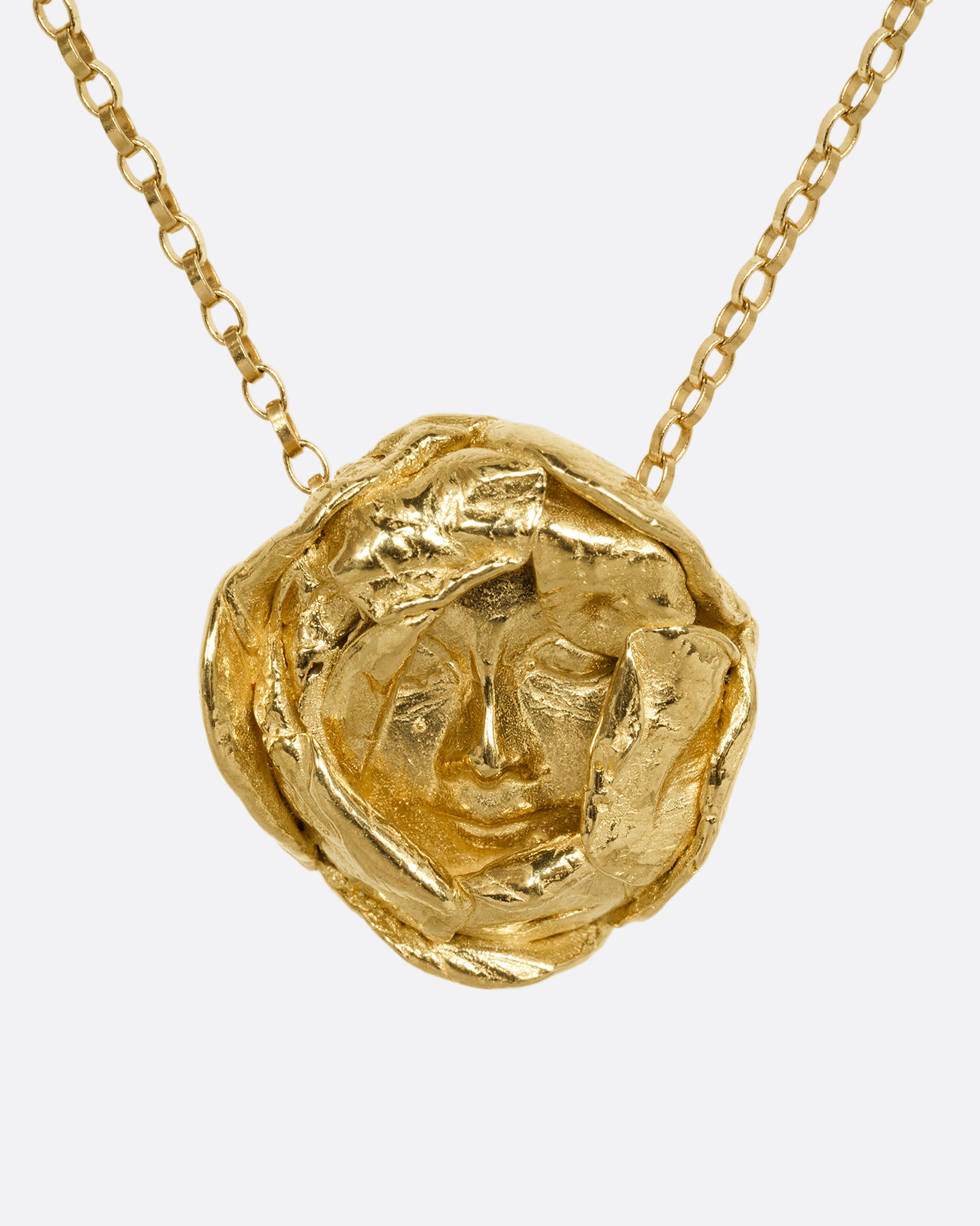 A yellow gold flower pendant with a sleeping face at its center on a cable chain. Shown from the front.