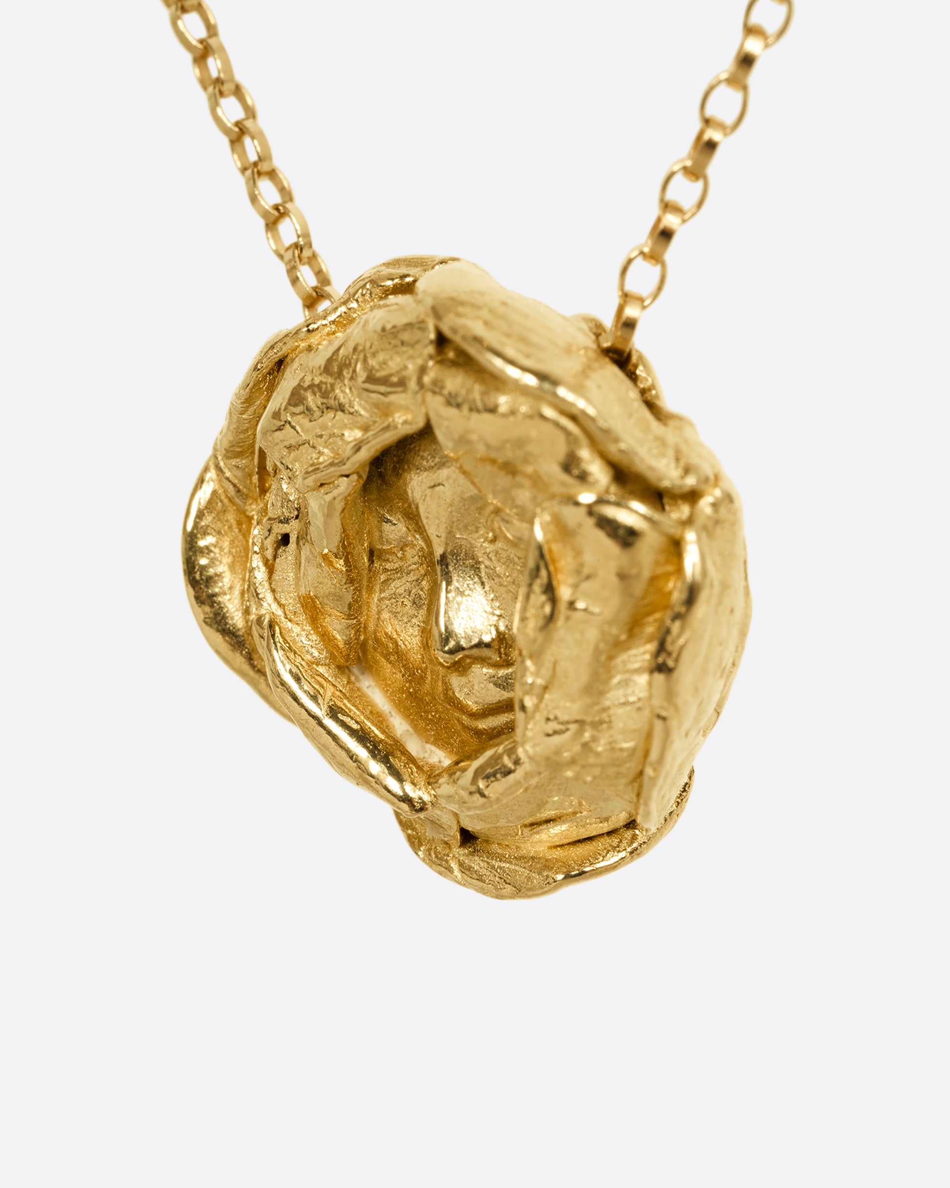 A yellow gold flower pendant with a sleeping face at its center on a cable chain. Shown from the side.