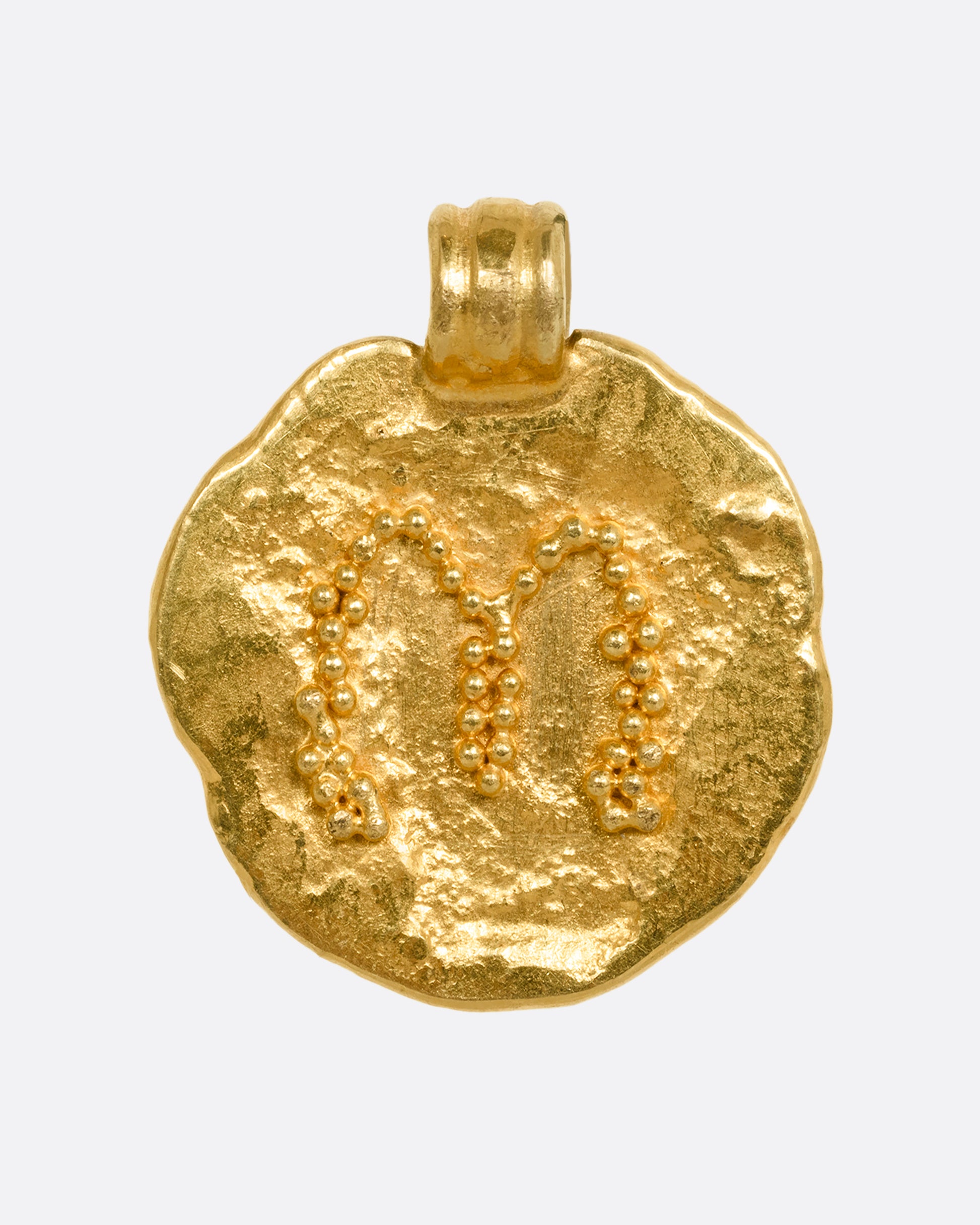 A high carat yellow gold organic circle pendant with the letter m on the face. Shown from the front.