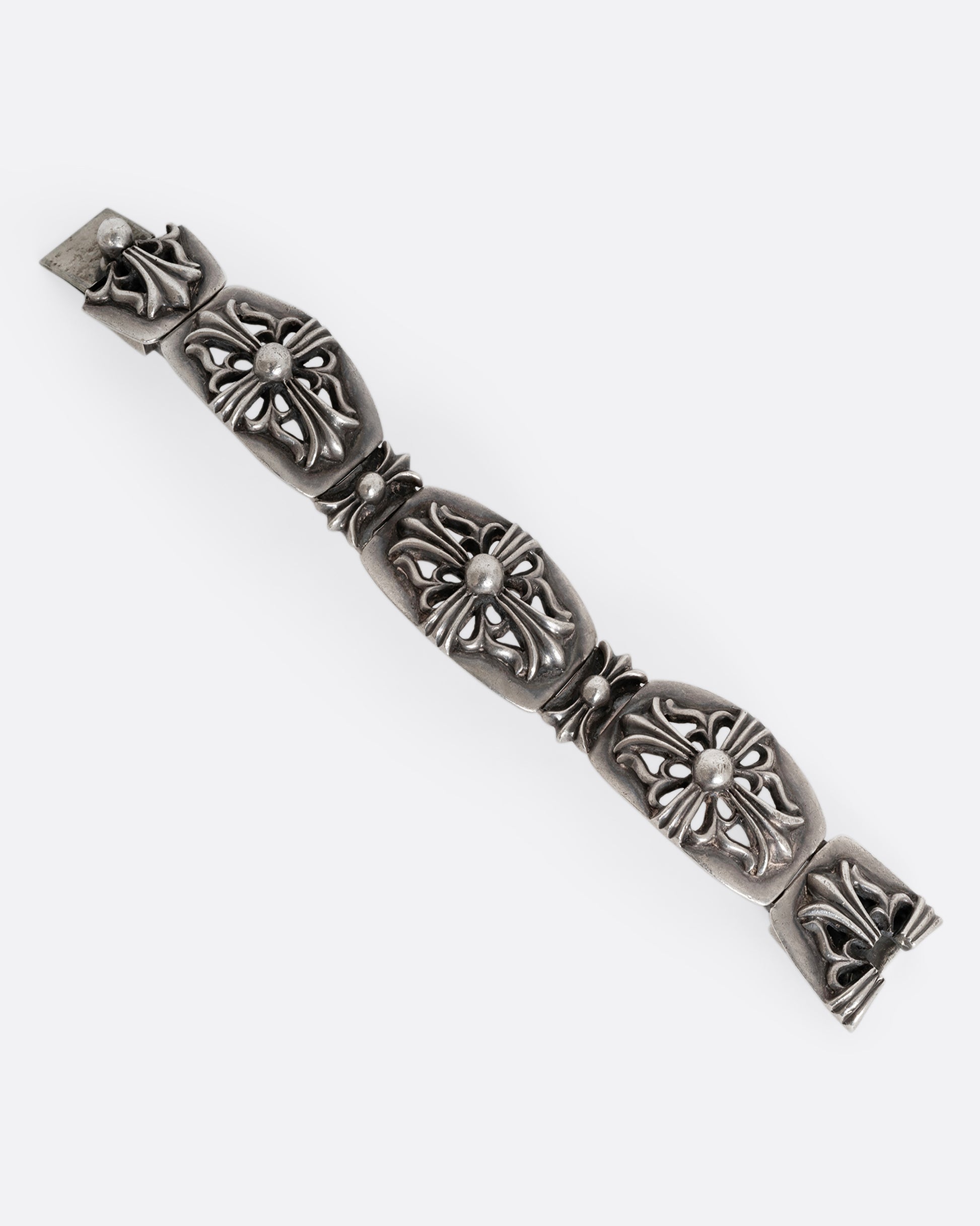 A sterling silver chunky bracelet from the brand Chrome Hearts with flower motifs on each link. Shown laying flat.