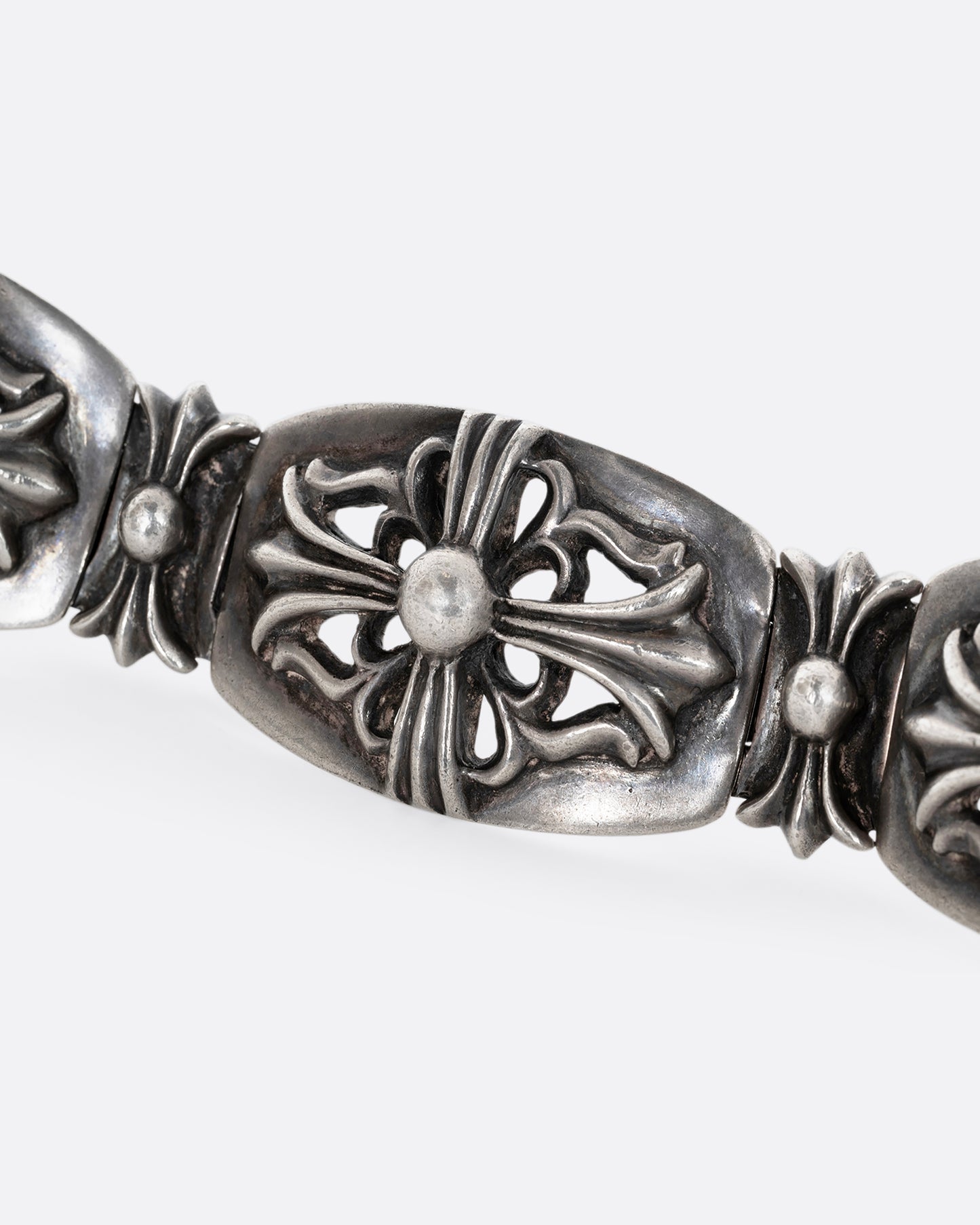 A sterling silver chunky bracelet from the brand Chrome Hearts with flower motifs on each link. Shown from the side, close up.