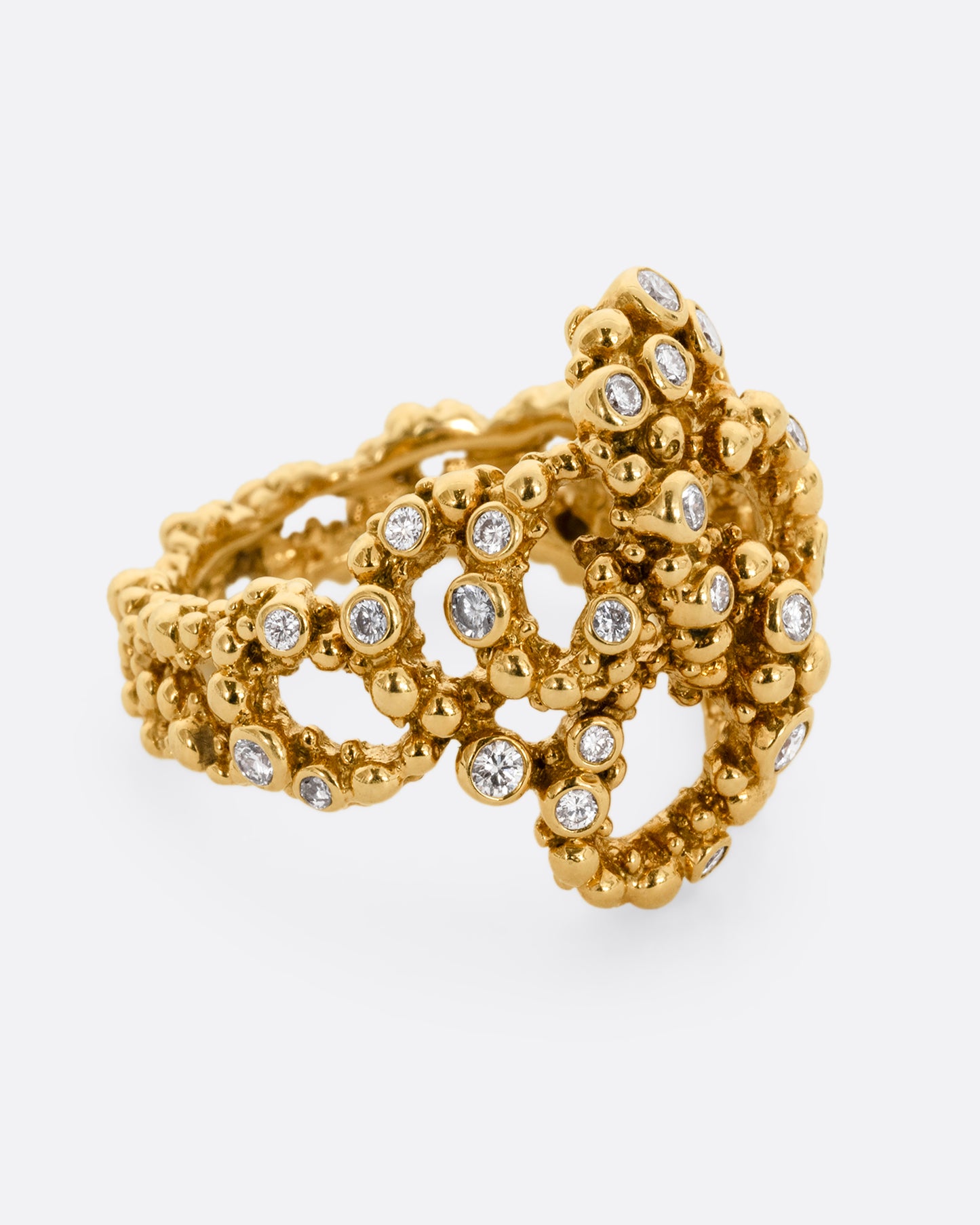 A yellow gold knotted ring with granule texture and diamonds throughout. Shown from the side.