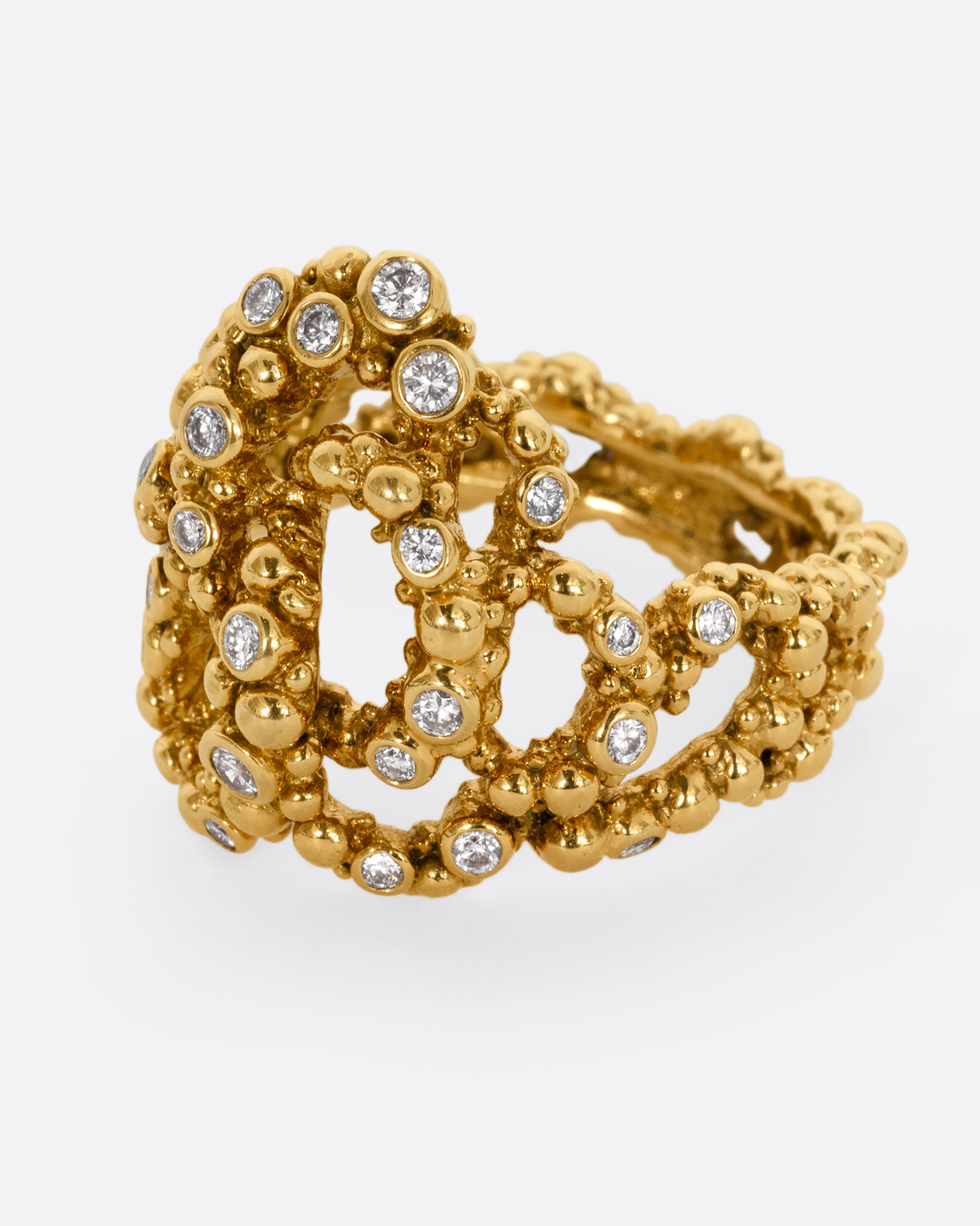 A yellow gold knotted ring with granule texture and diamonds throughout. Shown from the side.