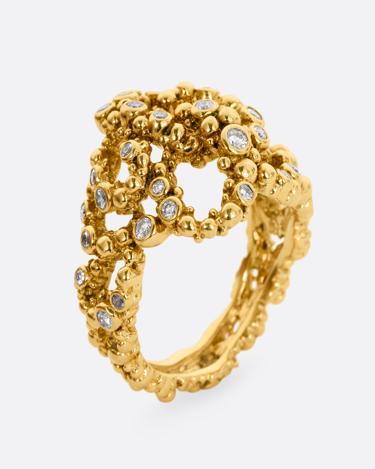 A yellow gold knotted ring with granule texture and diamonds throughout. Shown from the side, standing up.