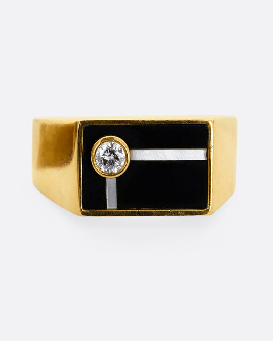 A yellow gold signet style ring with a black face, mother of pearl inlay and a single bezel set round diamond. Shown from the front.