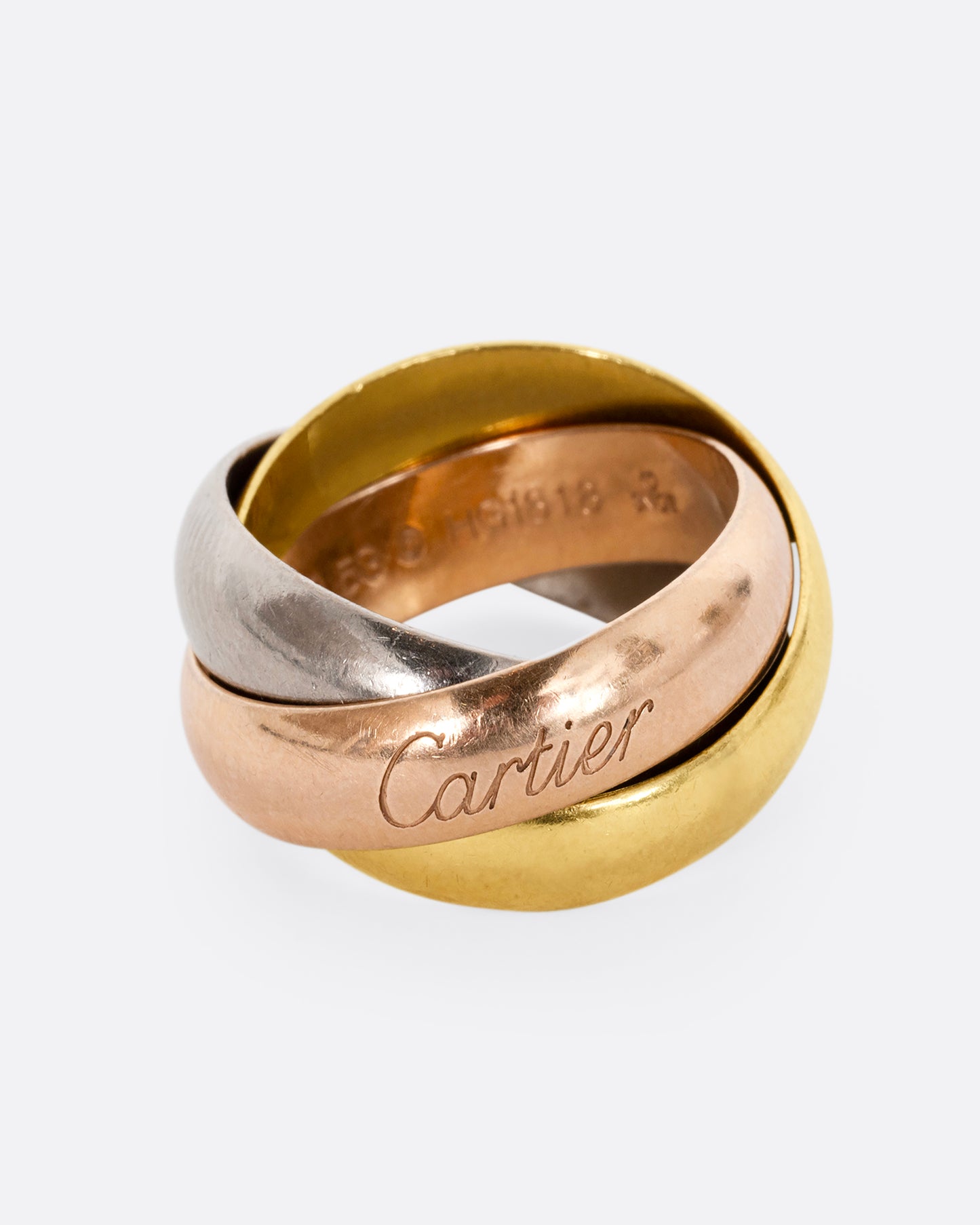 A yellow, rose and white gold wide rolling band from the heritage brand Cartier. Close up on the signature.