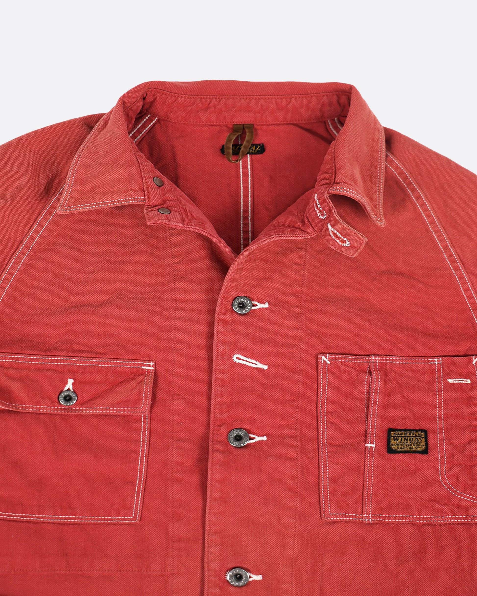 A red canvas chore coat with four front pockets. View close up of the collar.