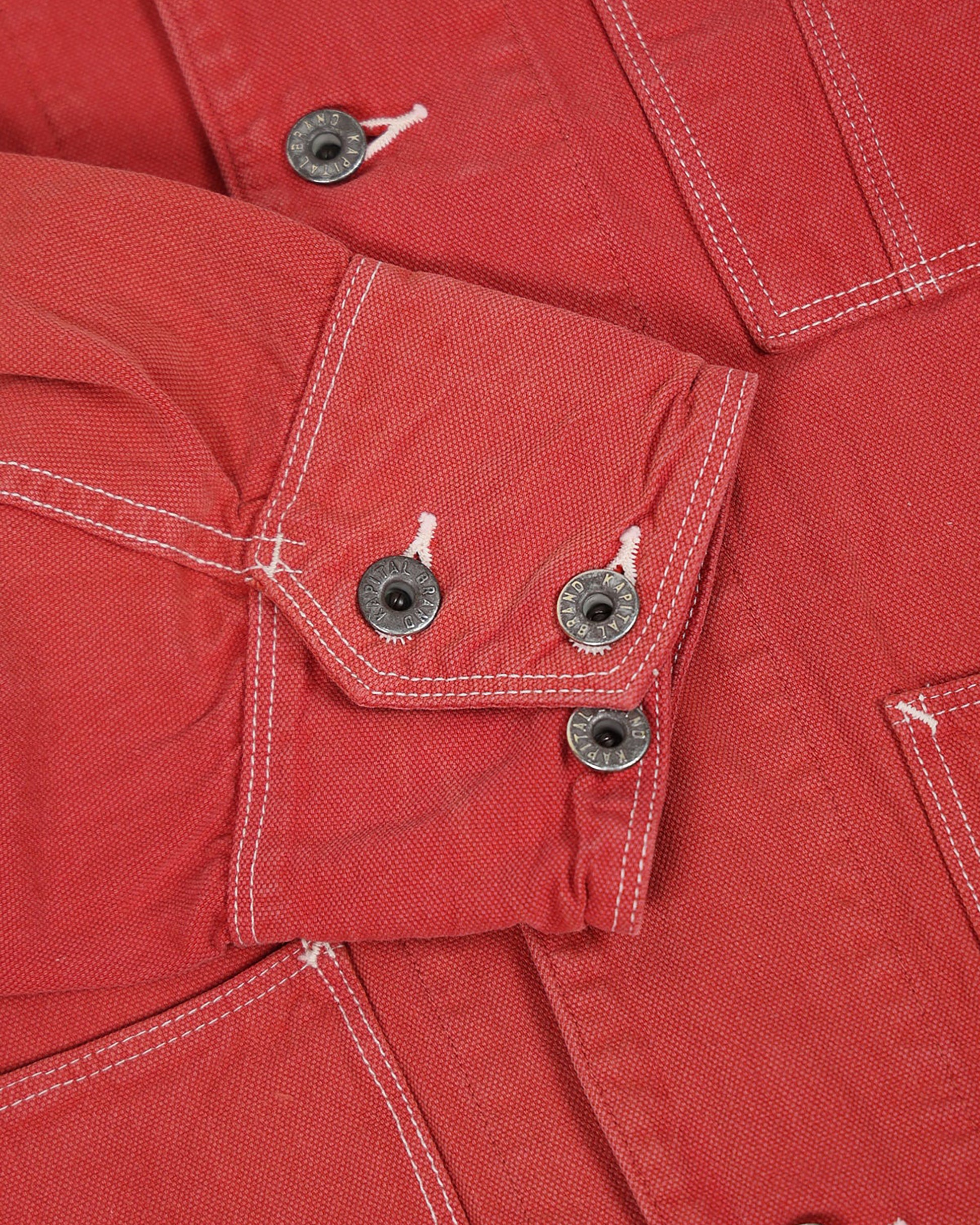 A red canvas chore coat with four front pockets. View of the cuff and contrast stitching.