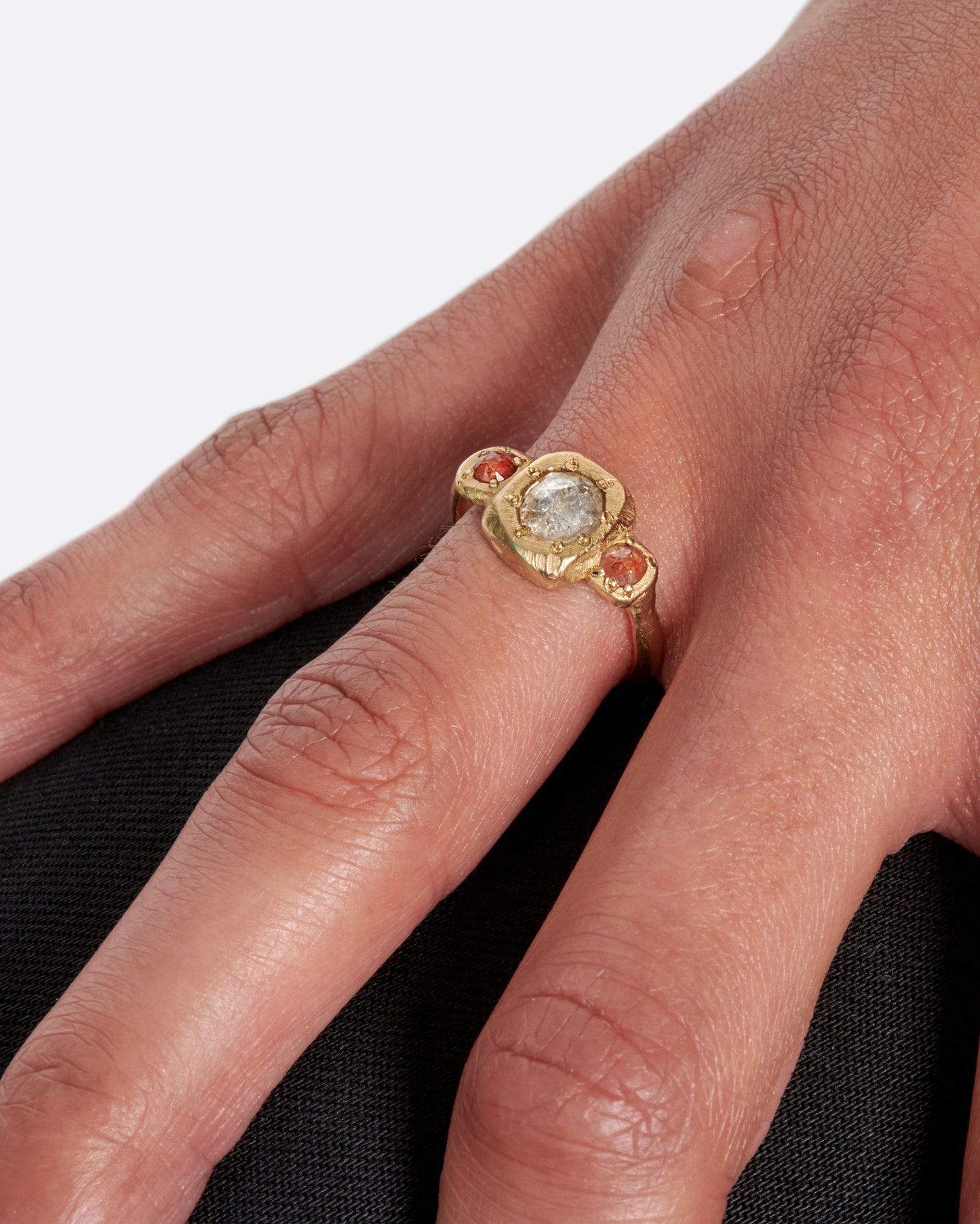 A one of a kind, organic take on a traditional three stone ring, featuring a rose cut grey diamond and two rose cut red diamonds, shown on a finger