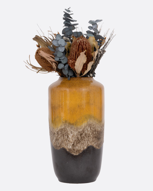 A tall ceramic vase with a ochre- to- brown gradient glaze, shown from the front with flowers.
