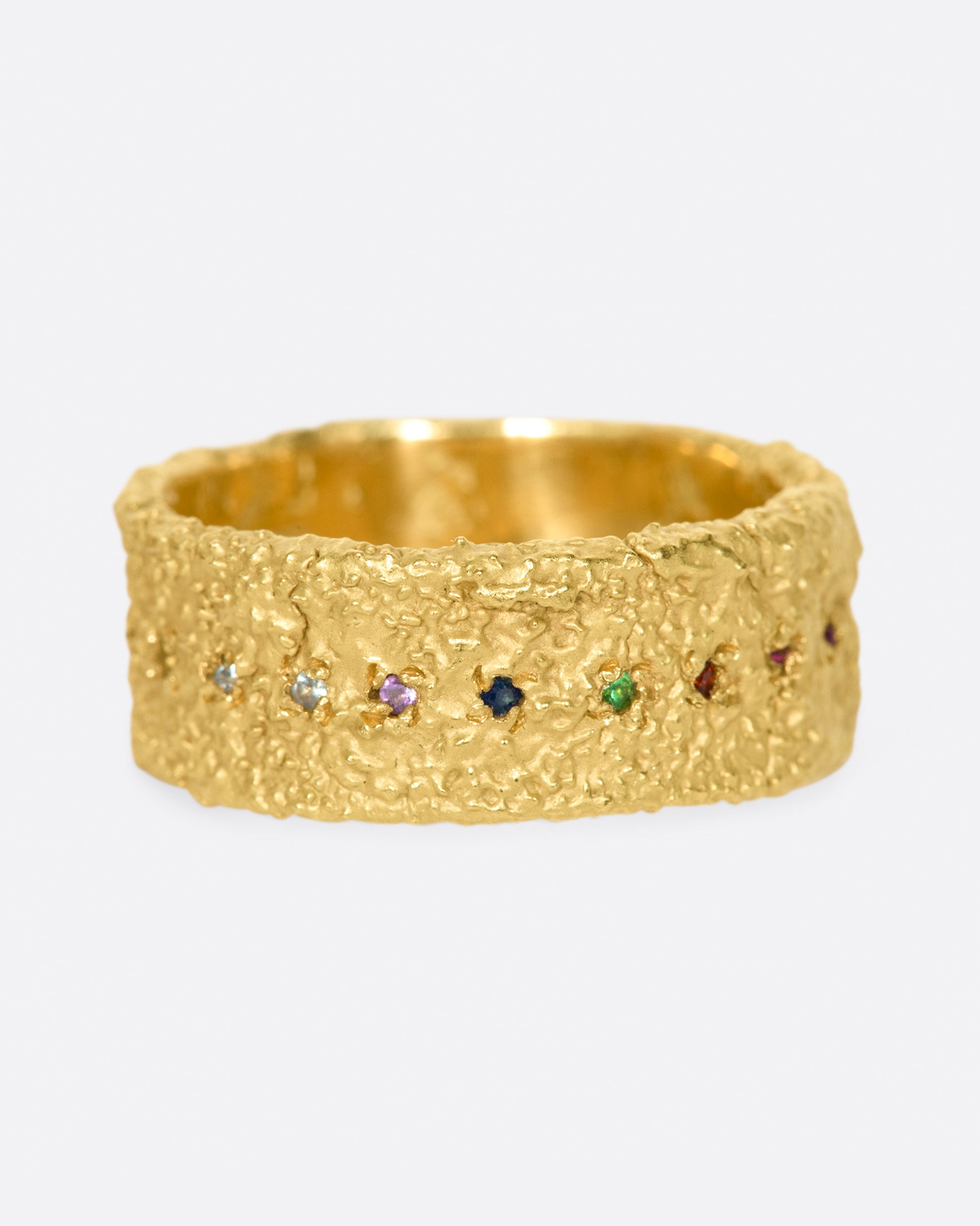 A wide textured band made with recycled yellow gold set with garnet, ruby, peridot, aquamarine, amethyst, emerald, and pink, orange, yellow and blue sapphires.