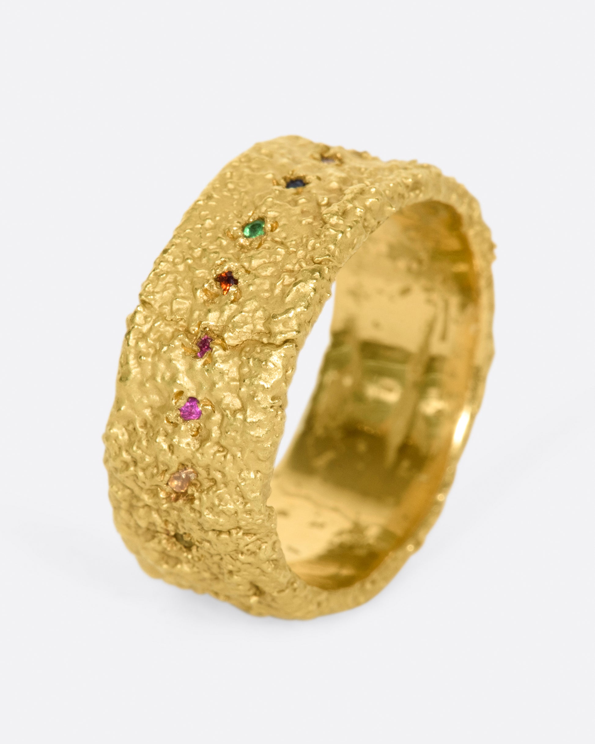 A wide textured band made with recycled yellow gold set with garnet, ruby, peridot, aquamarine, amethyst, emerald, and pink, orange, yellow and blue sapphires.