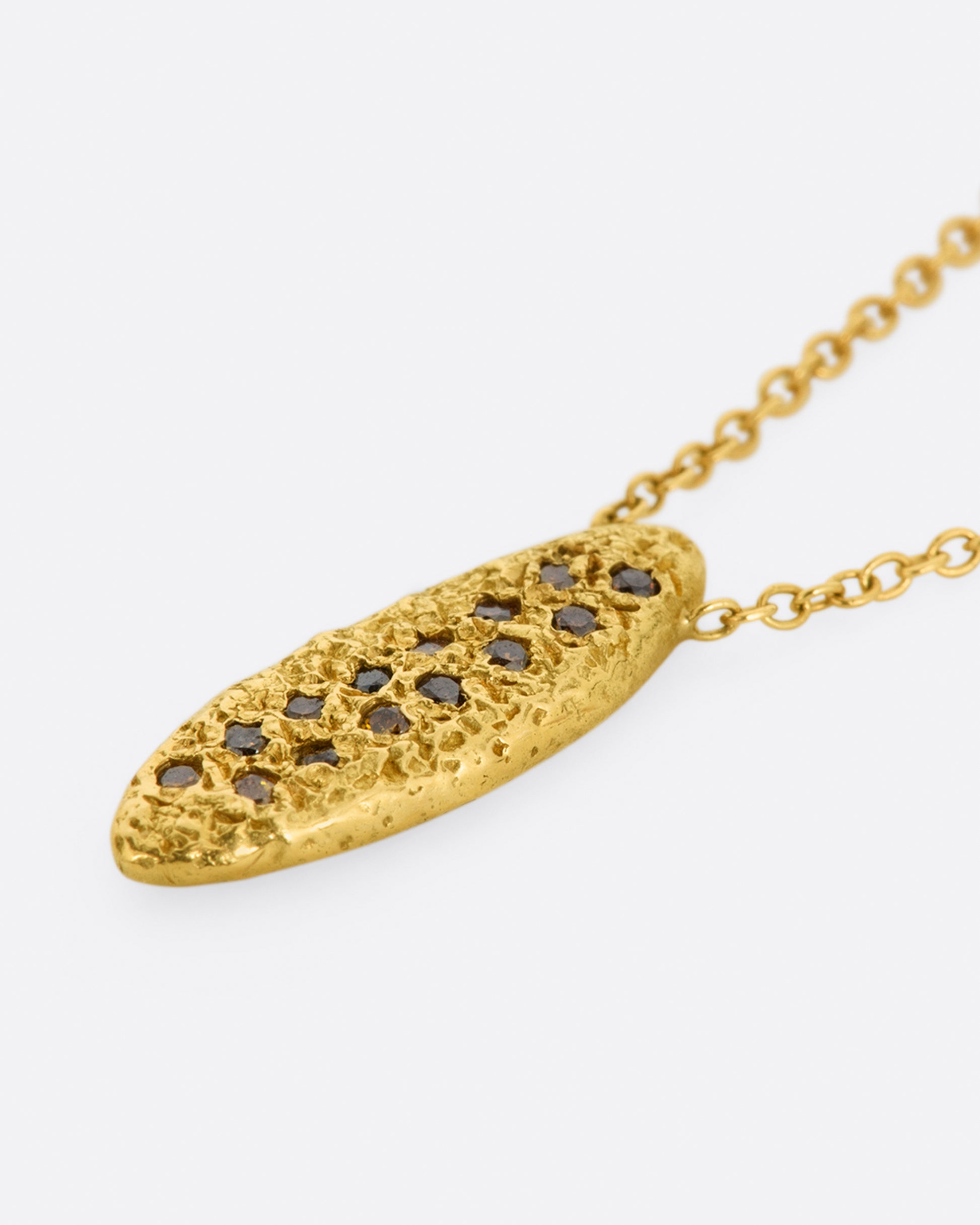 A yellow gold chain necklace with a marquise shape textured pendant, with two rows of red and brown diamonds. Shown from the side.