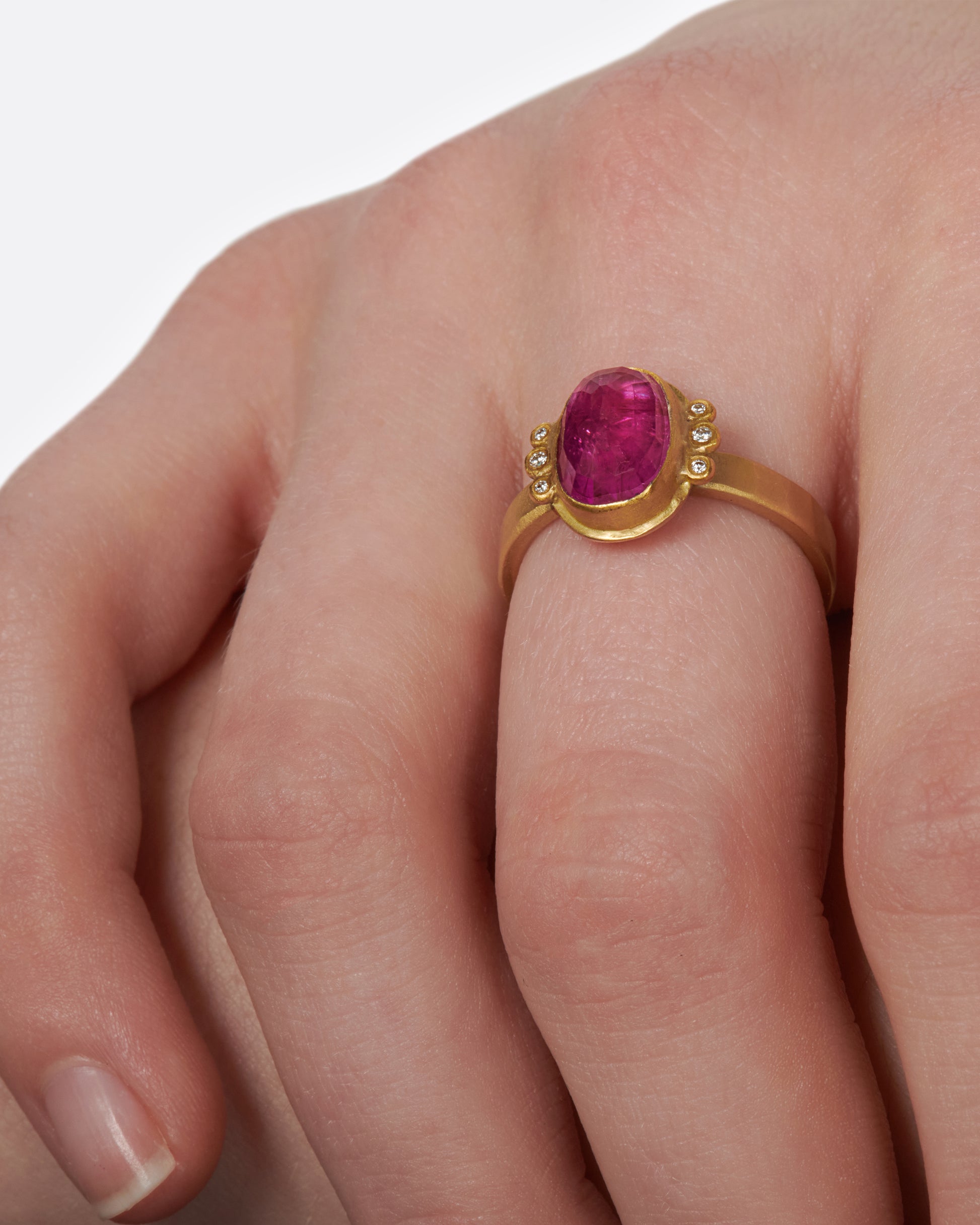 A saturated, faceted ruby shines in a high karat gold bezel with diamond accents.