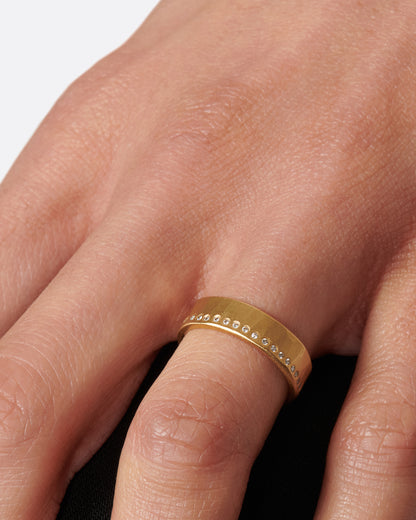 A hammered, matte gold band with a line of round diamonds all the way around. Shown on a hand.