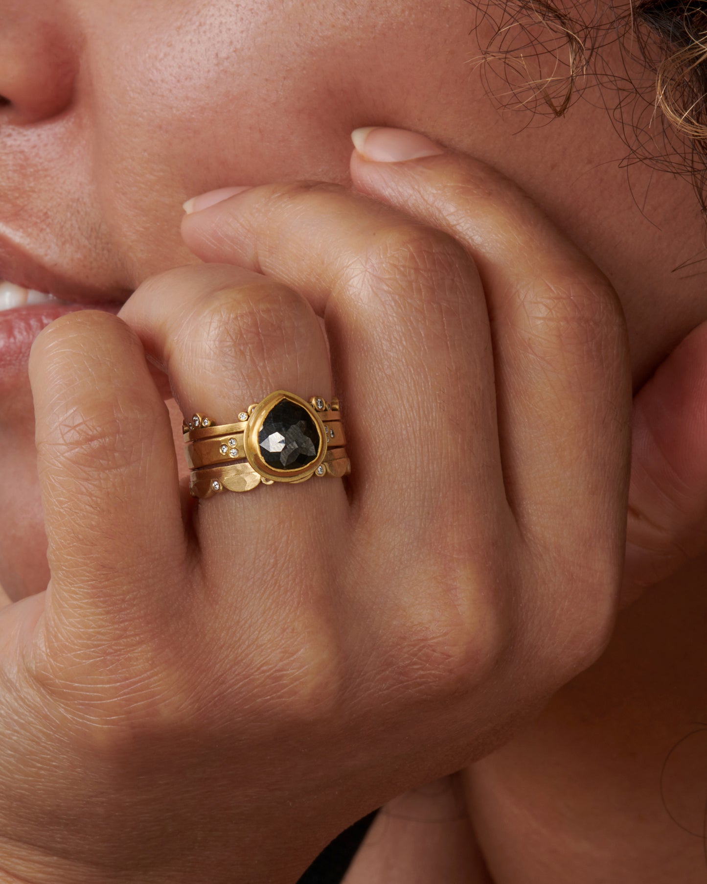 A matte gold band crowned with seven trios of diamonds, shown stacked with other rings.