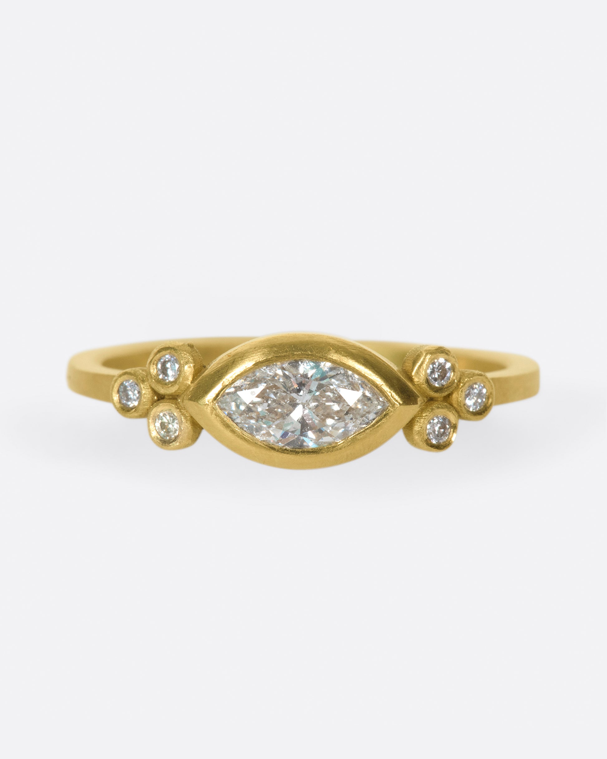 This ring features a sparkling, marquise diamond accented on each side by trios of tiny bezel set diamonds.