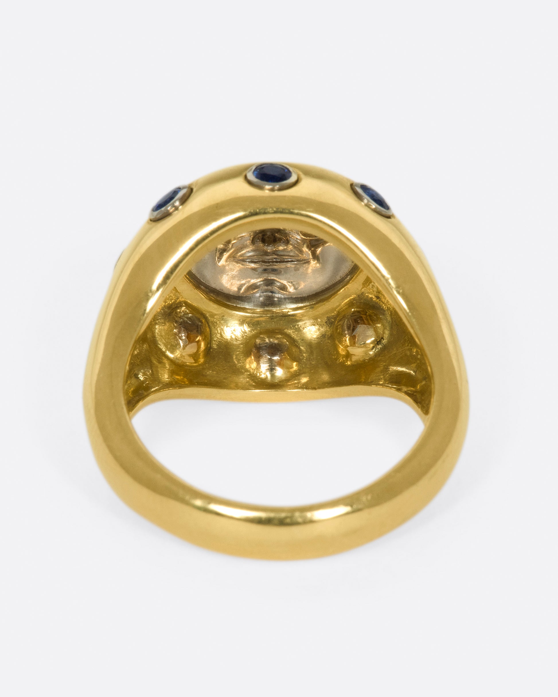 A platinum moonface sunken into a gold ring, surrounded by sapphire cabochons.