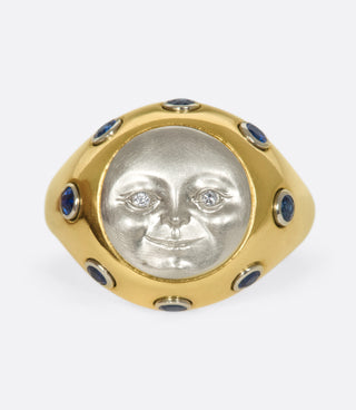 A platinum moonface sunken into a gold ring, surrounded by sapphire cabochons.