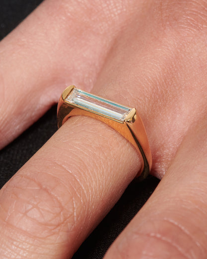 Yellow gold baguette diamond ring worn on a finger, the baguette diamond lying across the top