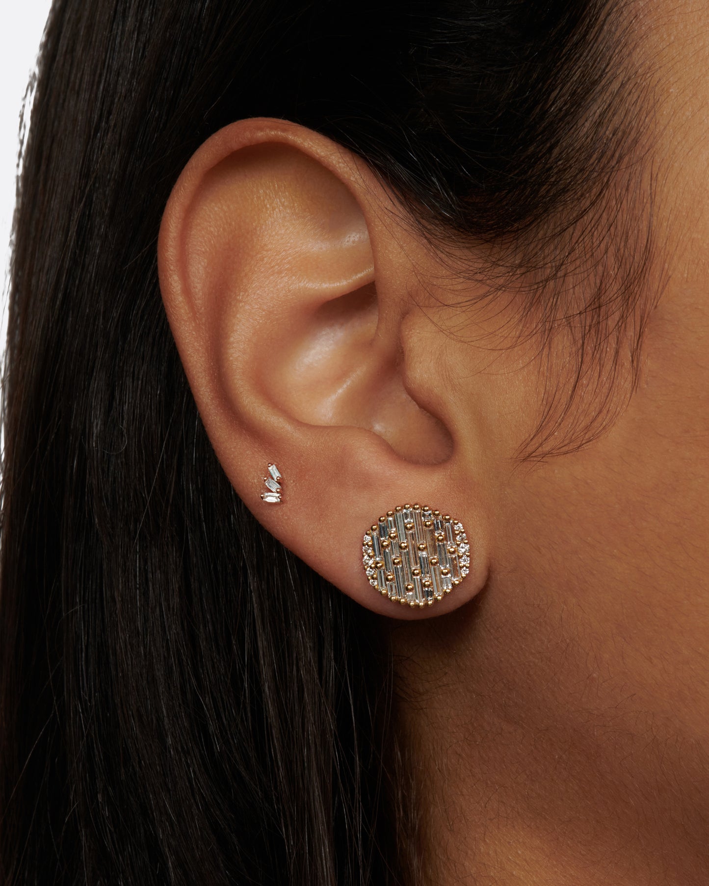 A pair of round, slightly concave stud earrings covered in baguette diamonds.