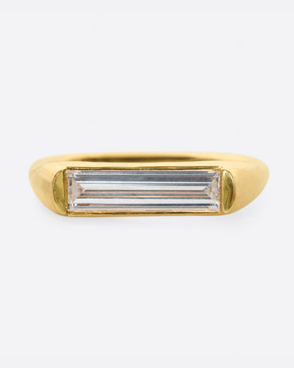 Artemer solitaire ring in yellow gold, a long baguette diamond set flat across the top of a slim band