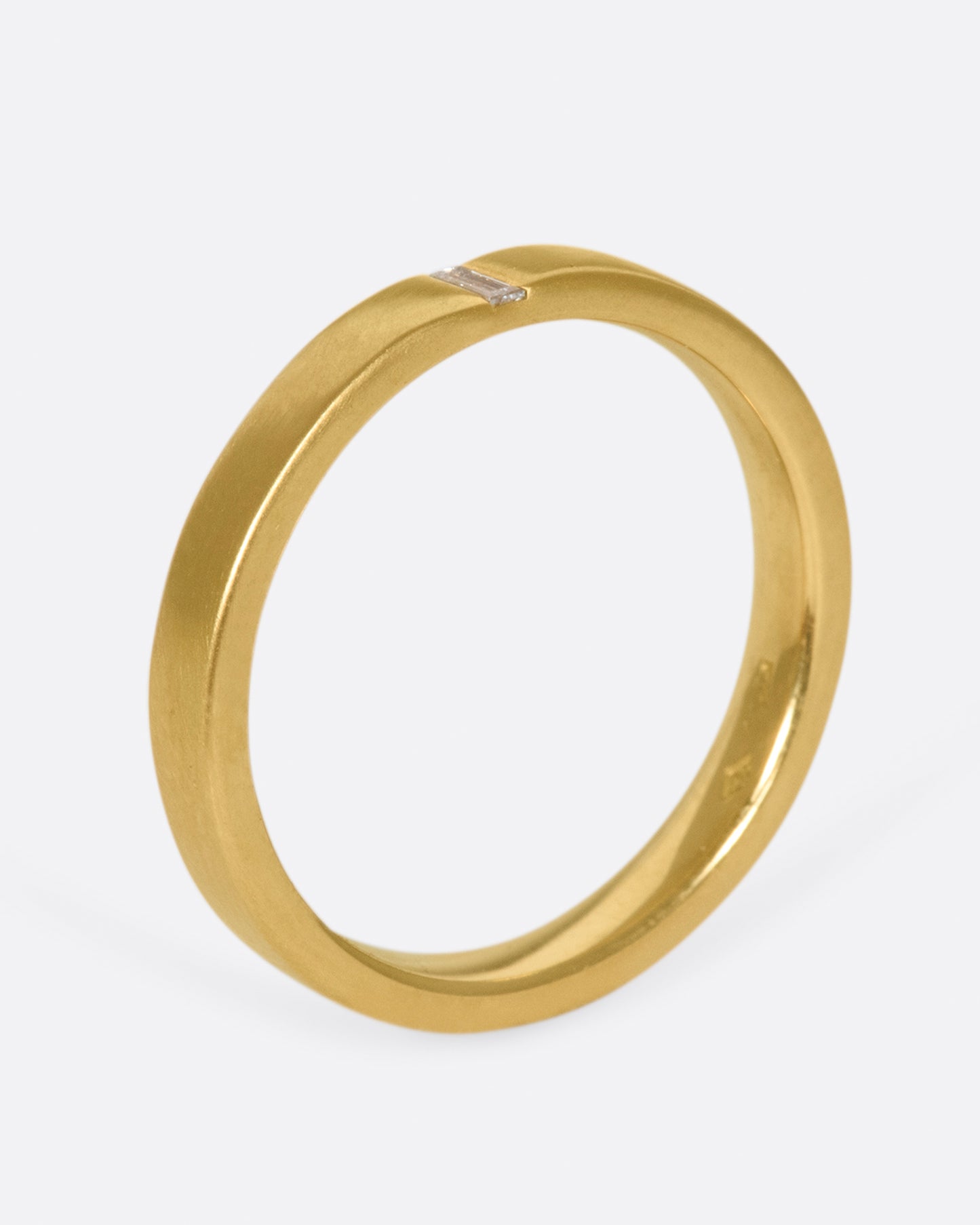 A matte gold band cast in a simple silhouette, featuring one needle baguette-cut diamond for that extra flare.