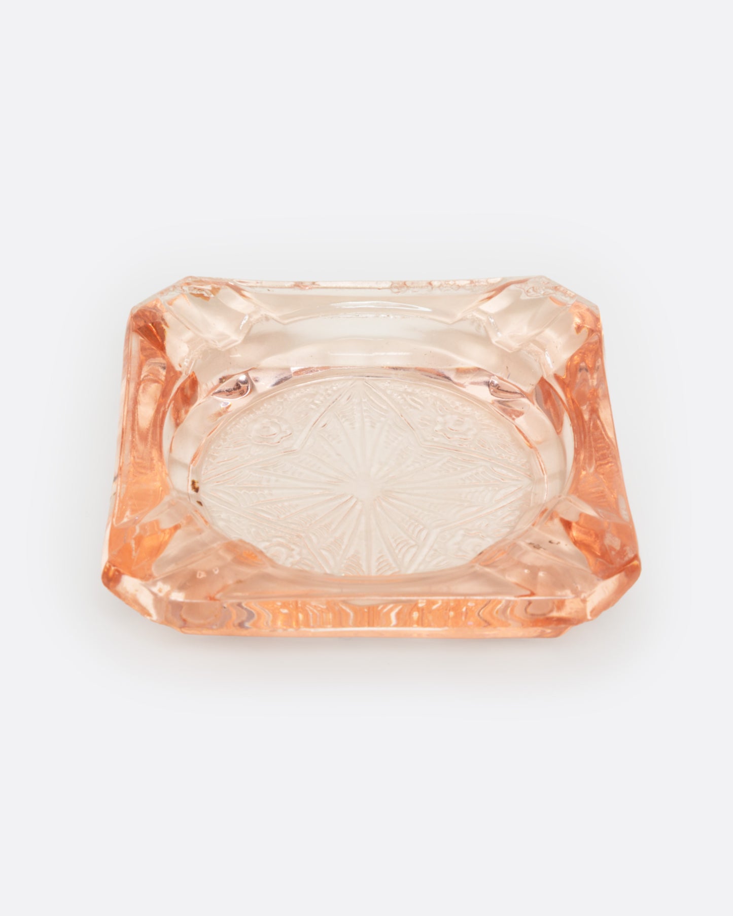 A peach glass ashtray with an etched starburst design, shown from the front.