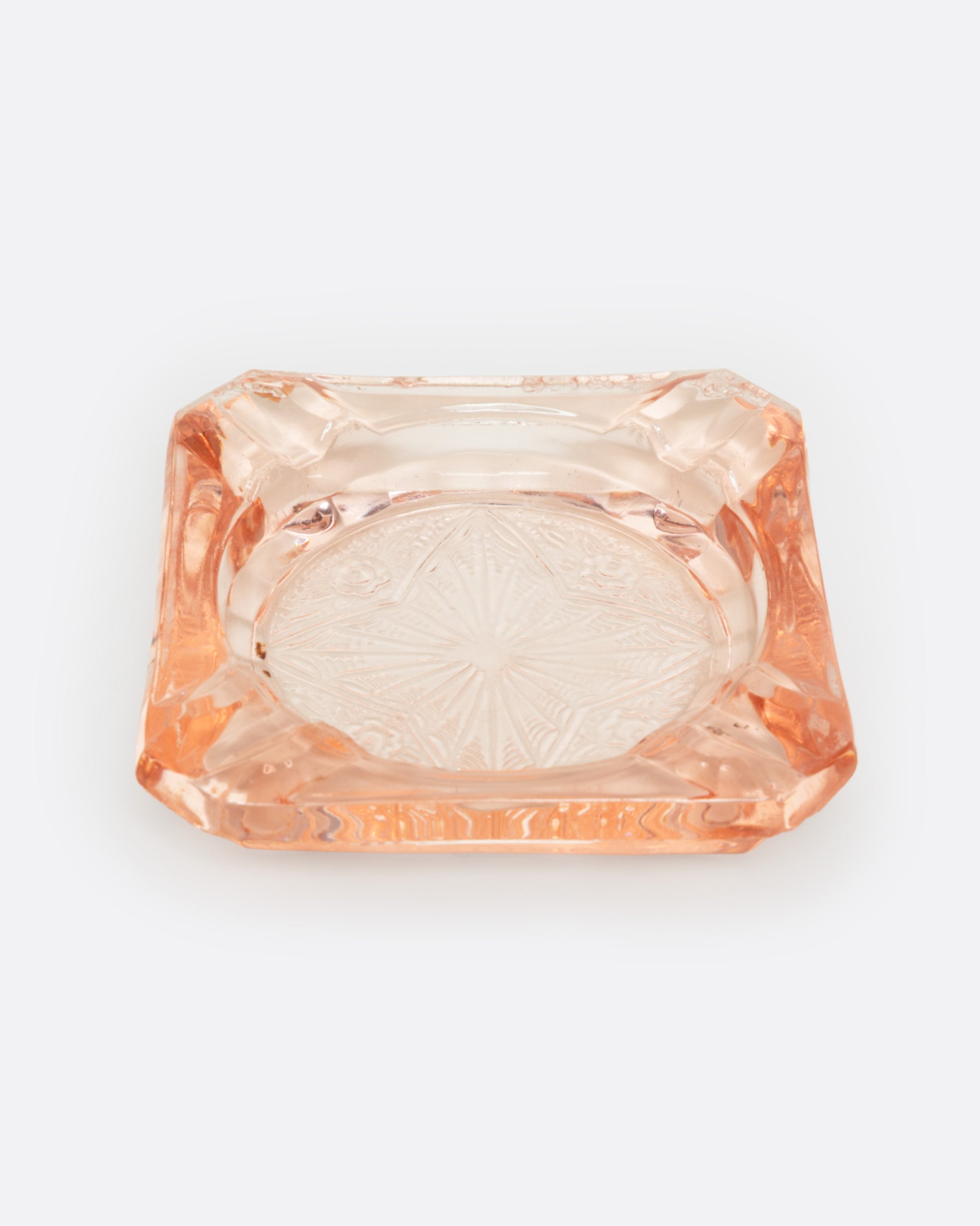A peach glass ashtray with an etched starburst design, shown from the front.