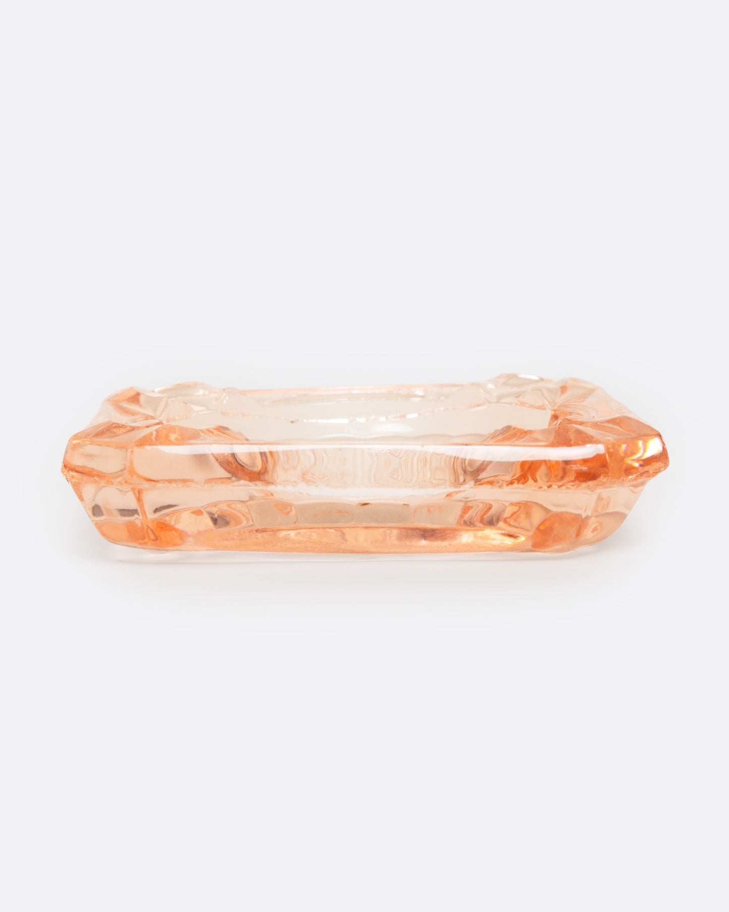 A peach glass ashtray with an etched starburst design, shown from the side.