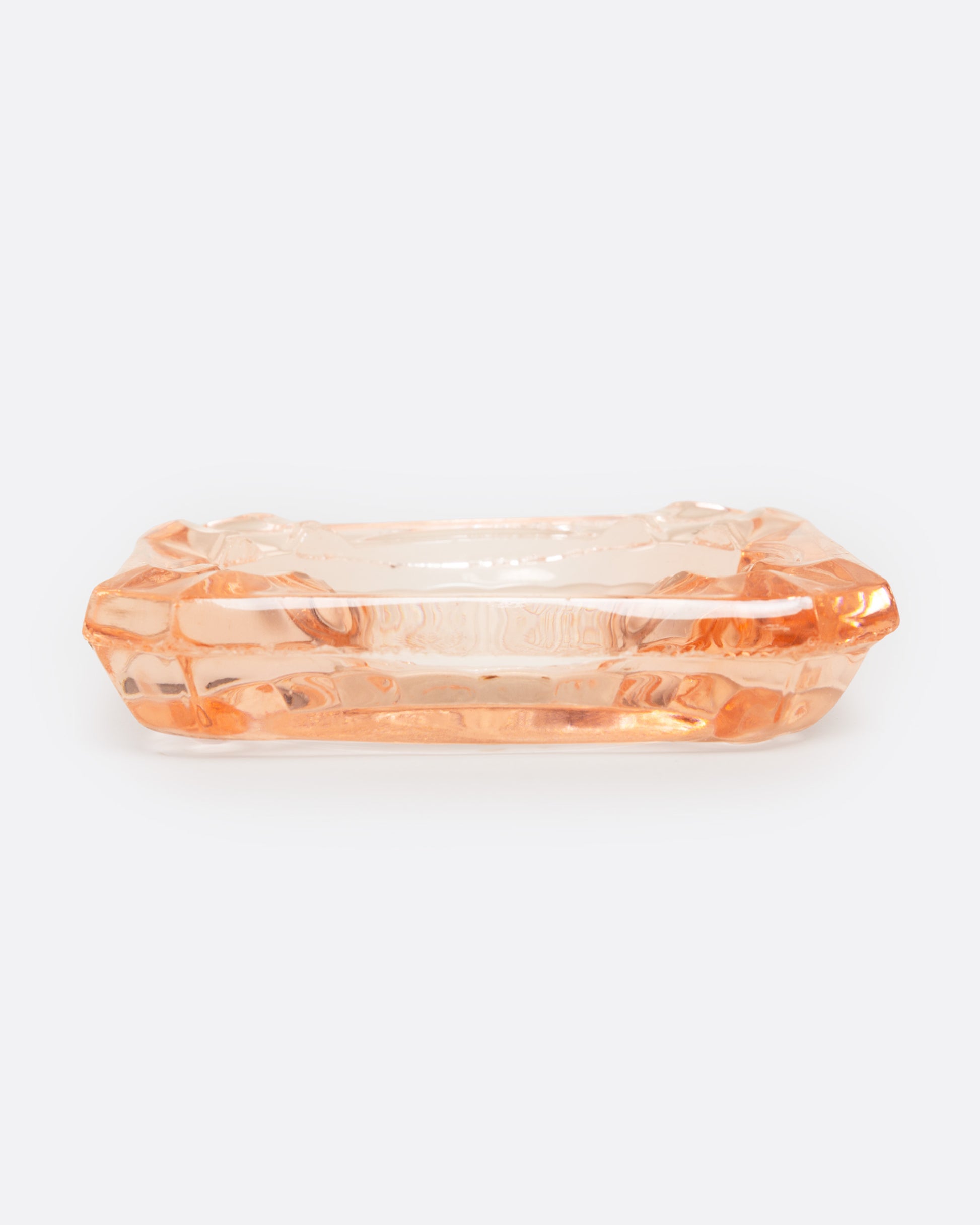 A peach glass ashtray with an etched starburst design, shown from the side.
