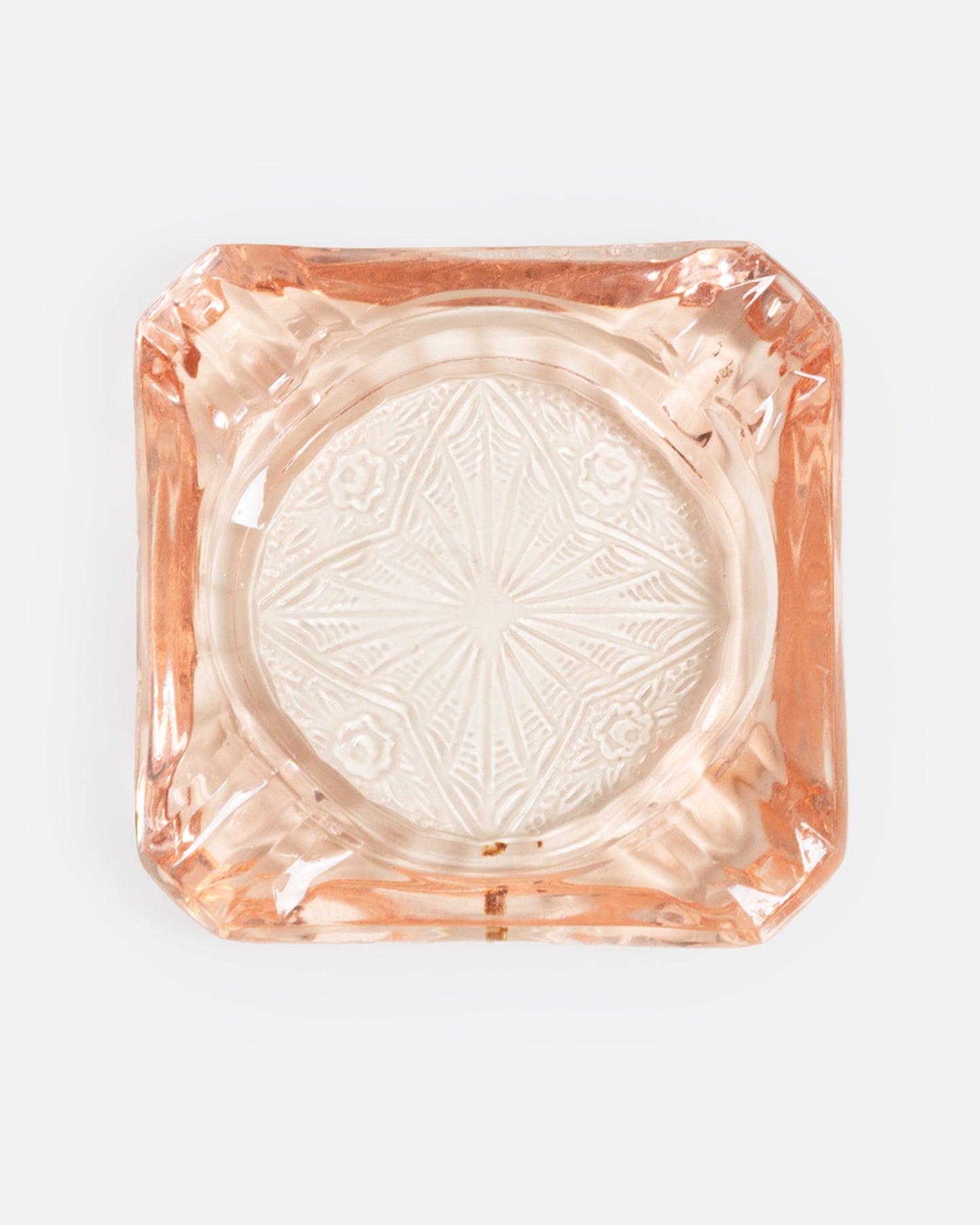 A peach glass ashtray with an etched starburst design, shown from the top.