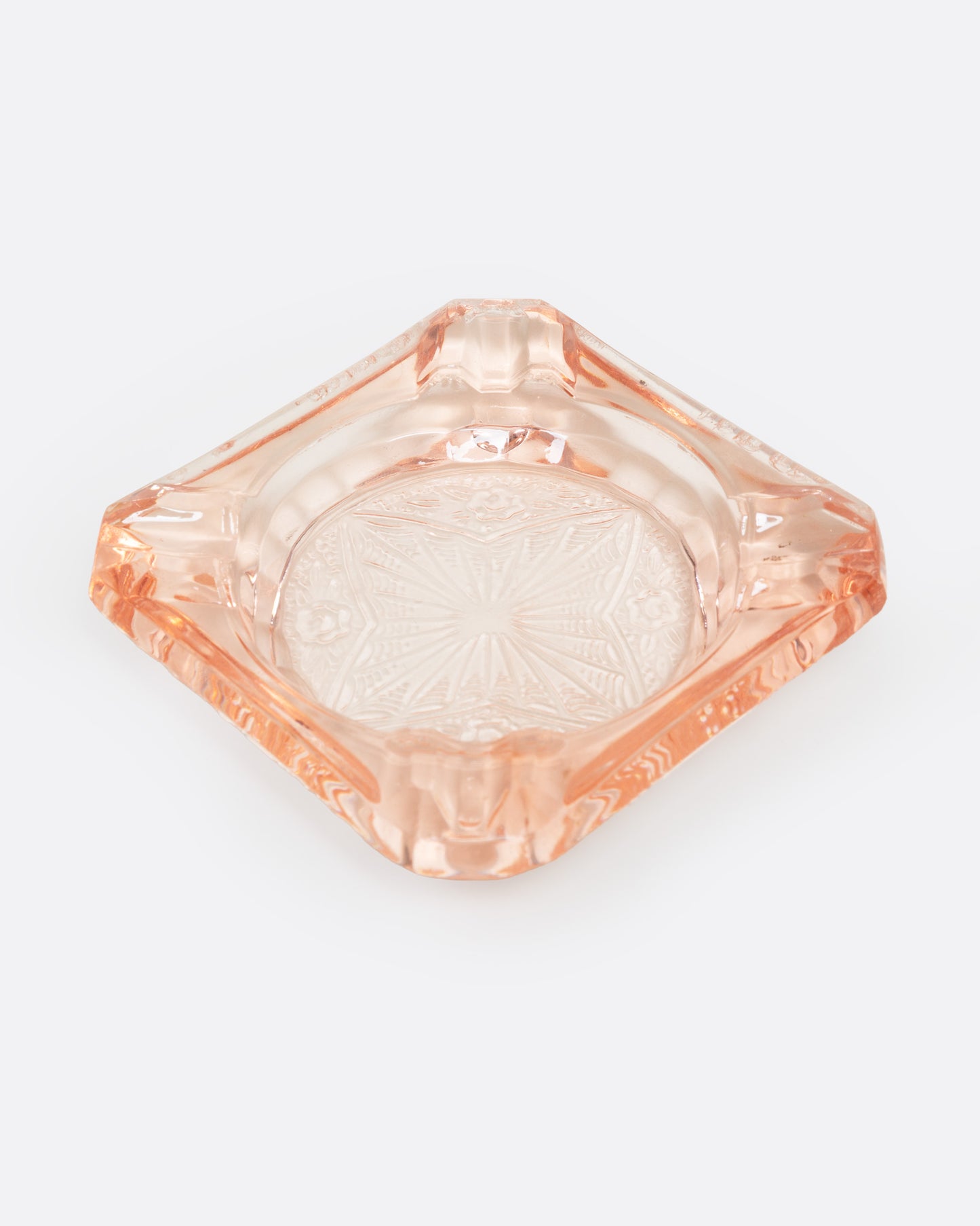 A peach glass ashtray with an etched starburst design, shown from the top.