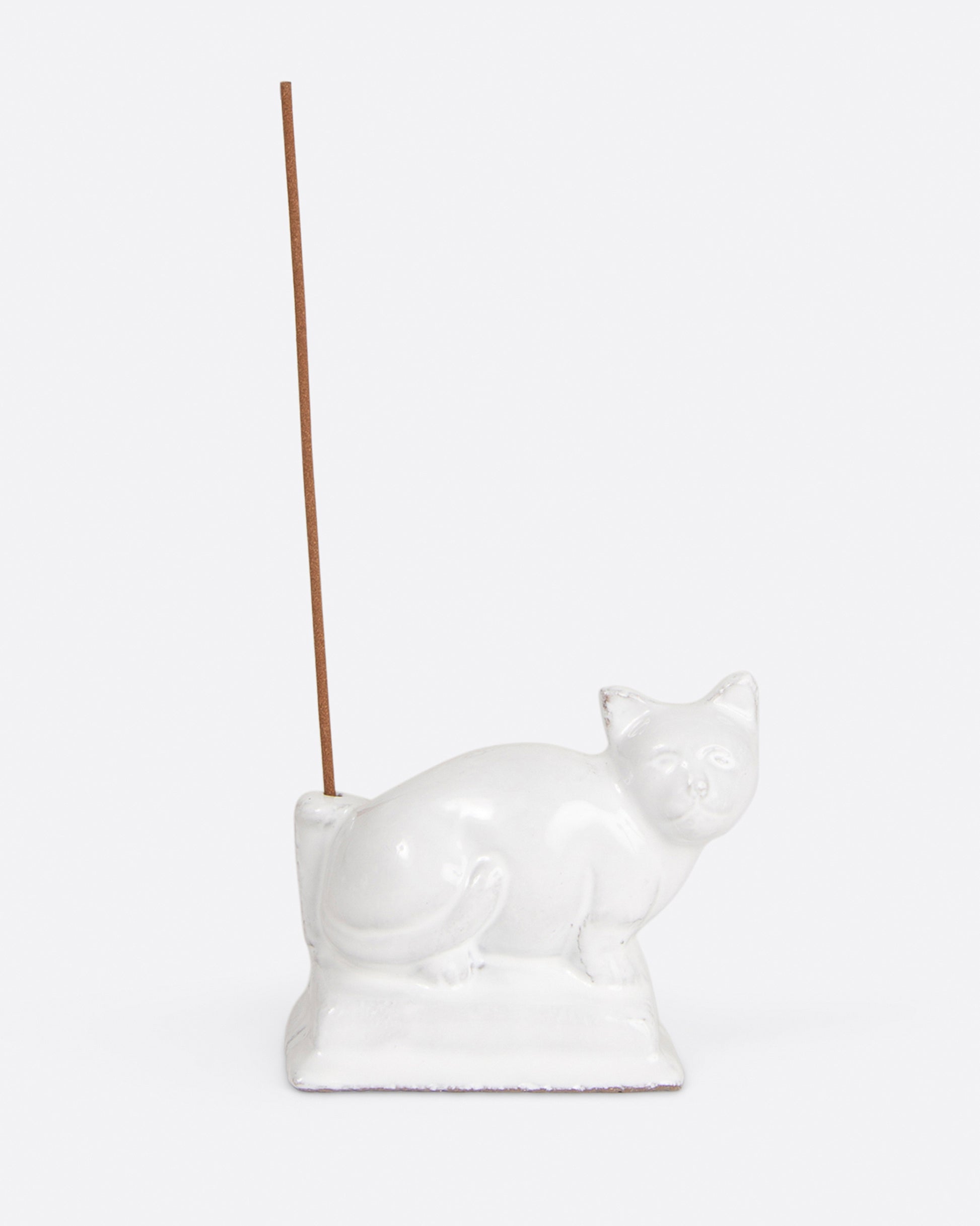 A glazed white ceramic cat-shaped incense holder with a stick of incense, shown from the front.