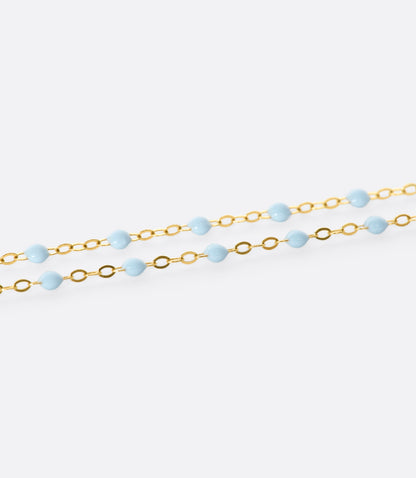 A close up view of a yellow gold cable chain necklace with baby blue resin droplets. Shown from the side.