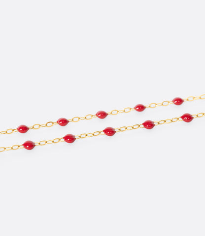 A close up view of a yellow gold cable chain necklace with red resin droplets. Shown from the side.