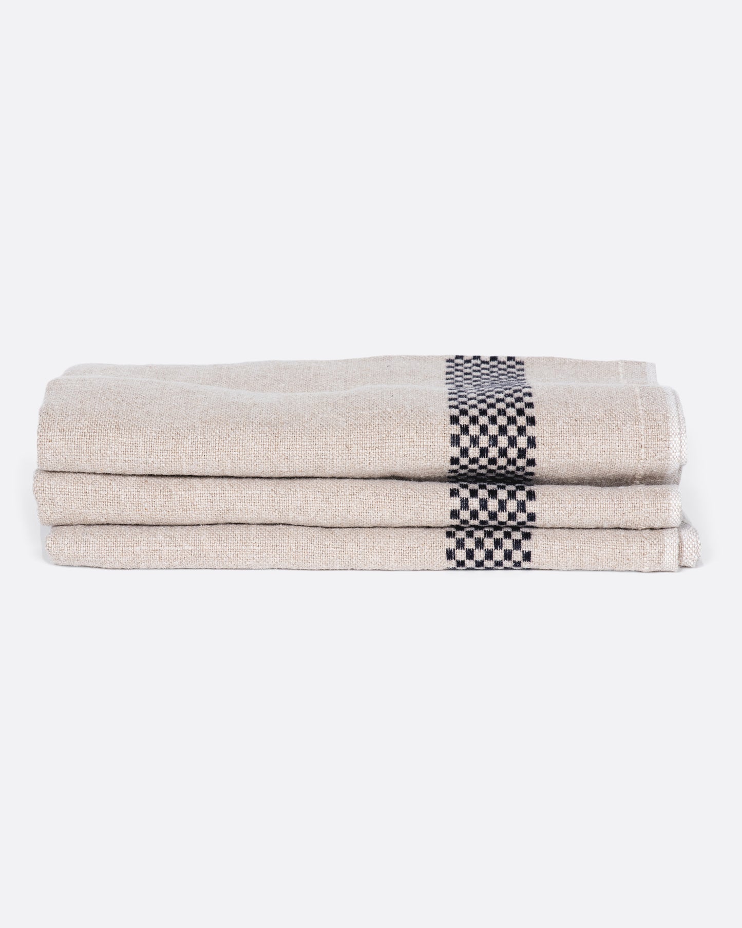 A stack of three natural linen napkins with black checkered embroidery