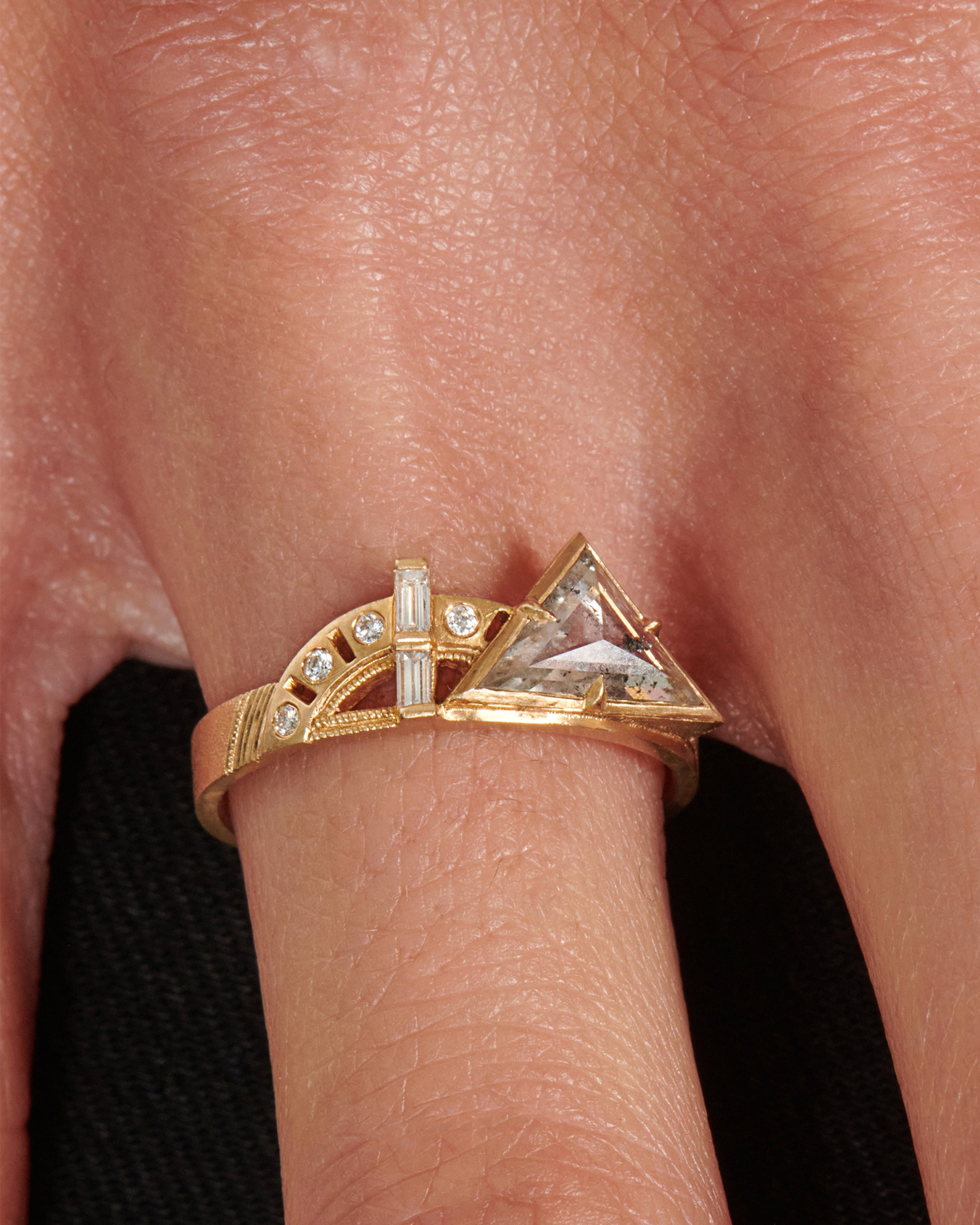 A wide flat band with a salt & pepper trillion cut diamond, gold arches, and round and baguette diamonds at its center.