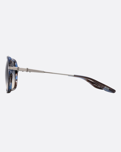 A pair of navigator sunglasses  with pearly blue and silver structured frames and gray gradient lenses. Shown from the side.