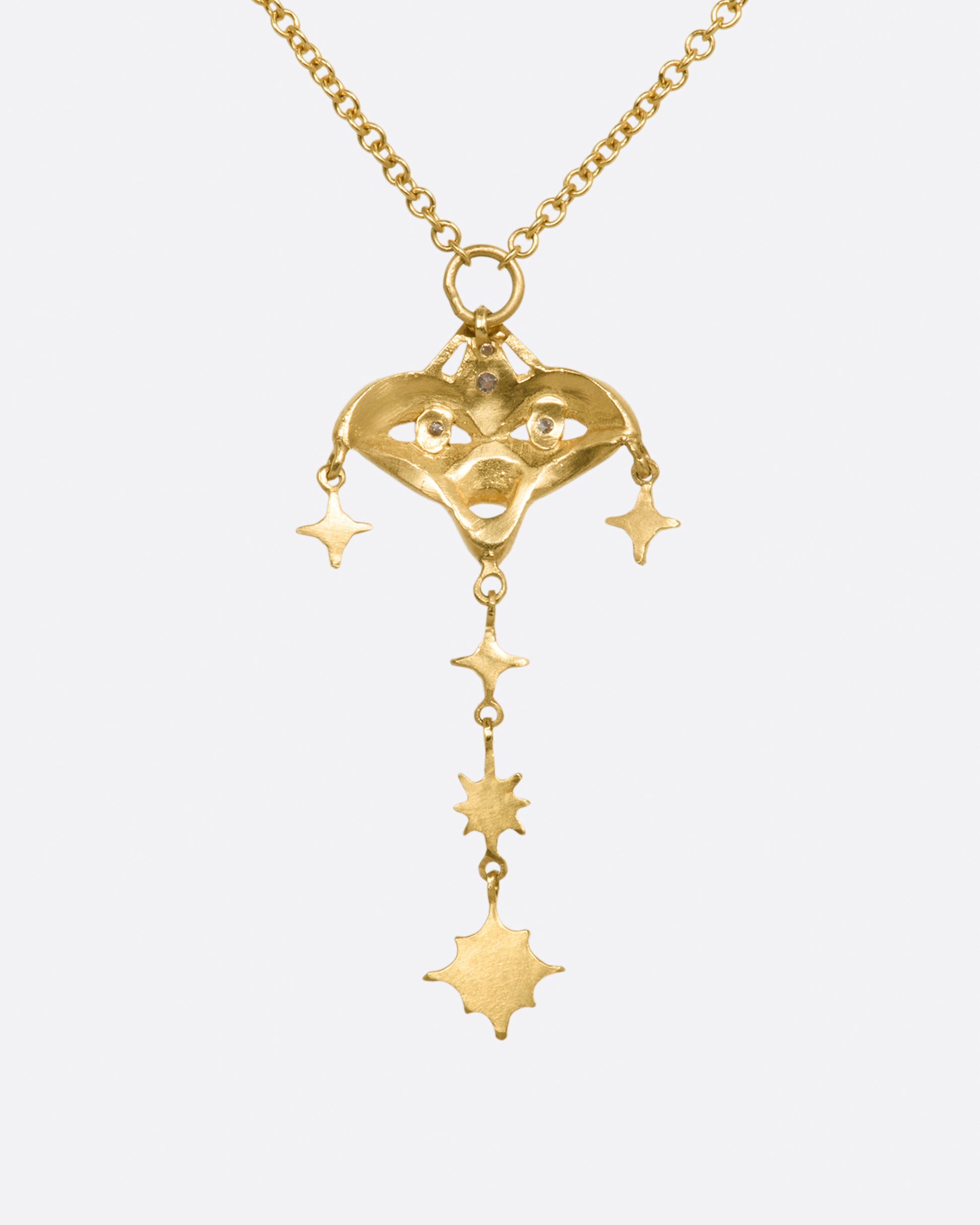 A yellow gold necklace with a mask pendant with diamond eyes and various star dangles, shown from the back.