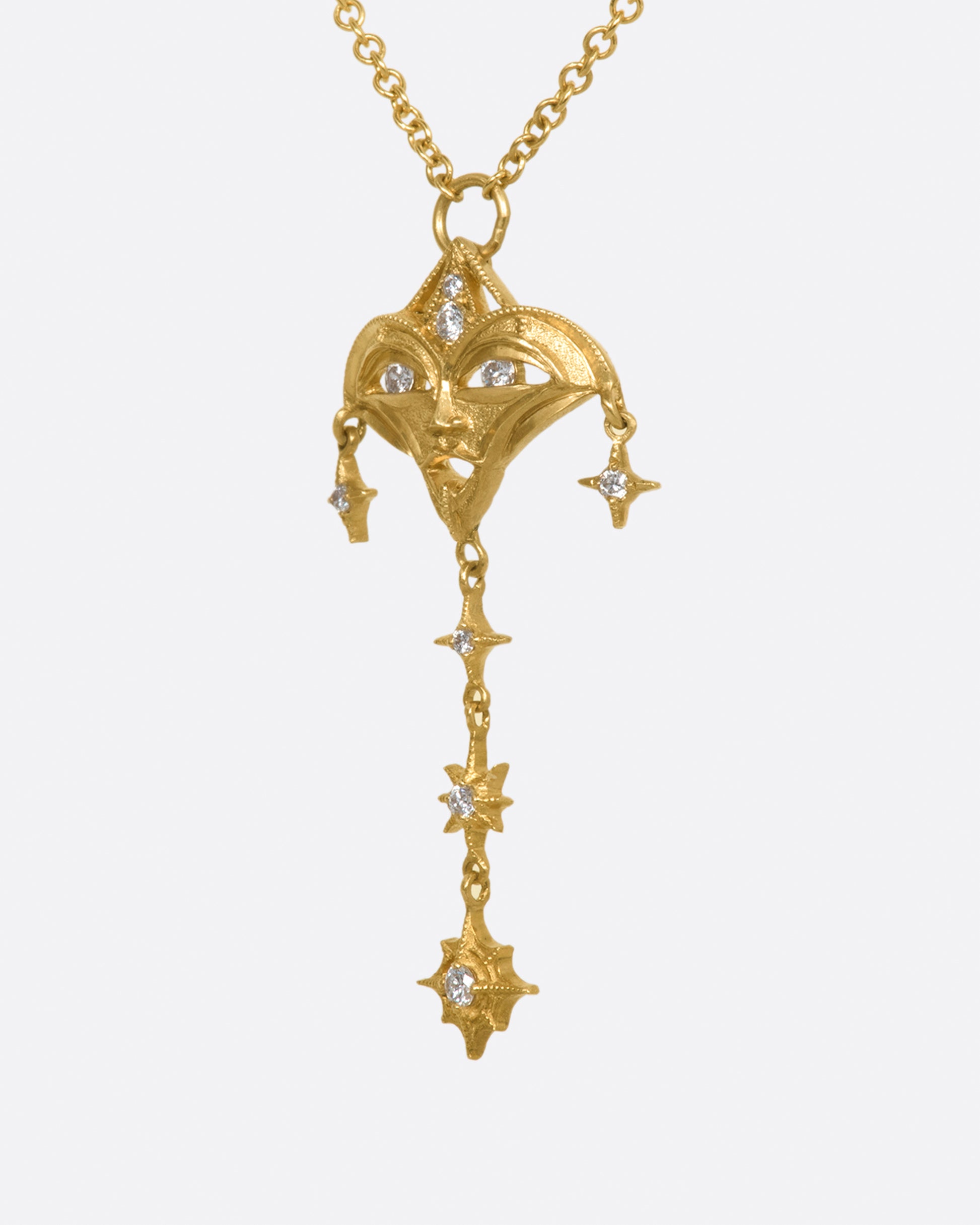 A yellow gold necklace with a mask pendant with diamond eyes and various star dangles, shown from the side.