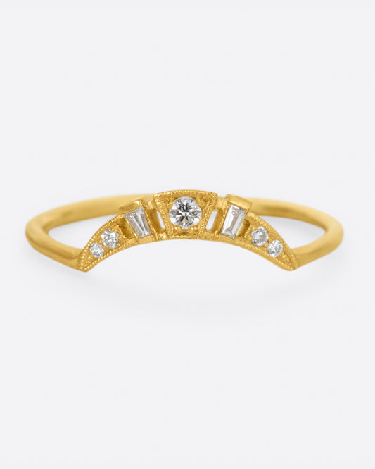 A yellow gold ring with a curved face that makes it good for stacking, dotted with round and baguette diamonds, and milgrain details.