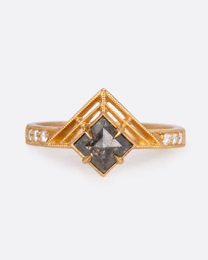A yellow gold ring with a central black diamond with white diamond details on both sides of the band. Shown from the front.