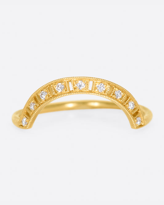 A yellow gold ring with a curved face that makes it good for stacking, dotted with round diamonds, cutouts and milgrain details.